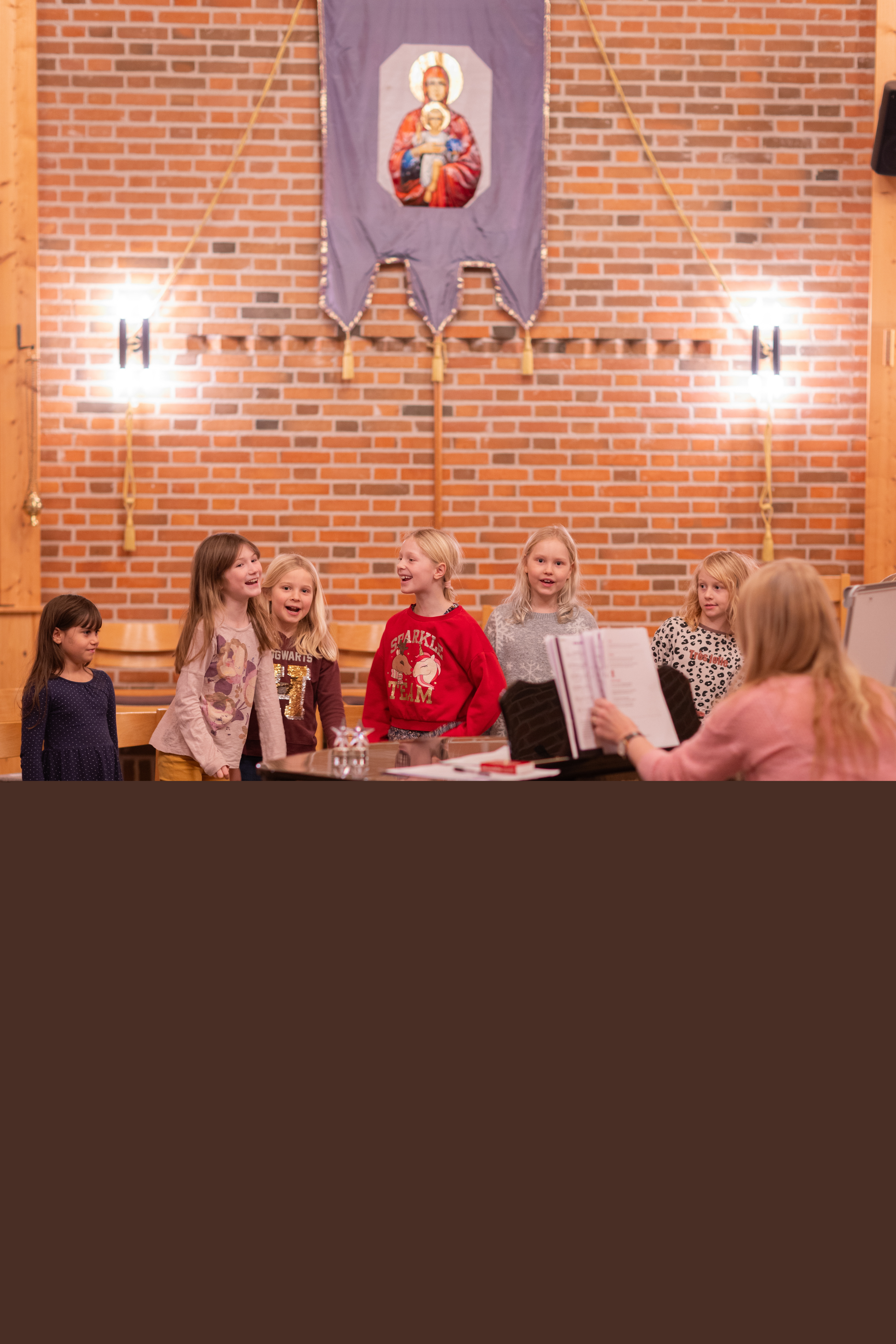 En grupp barn står runt en flygel i en kyrka och skrattar och sjunger.