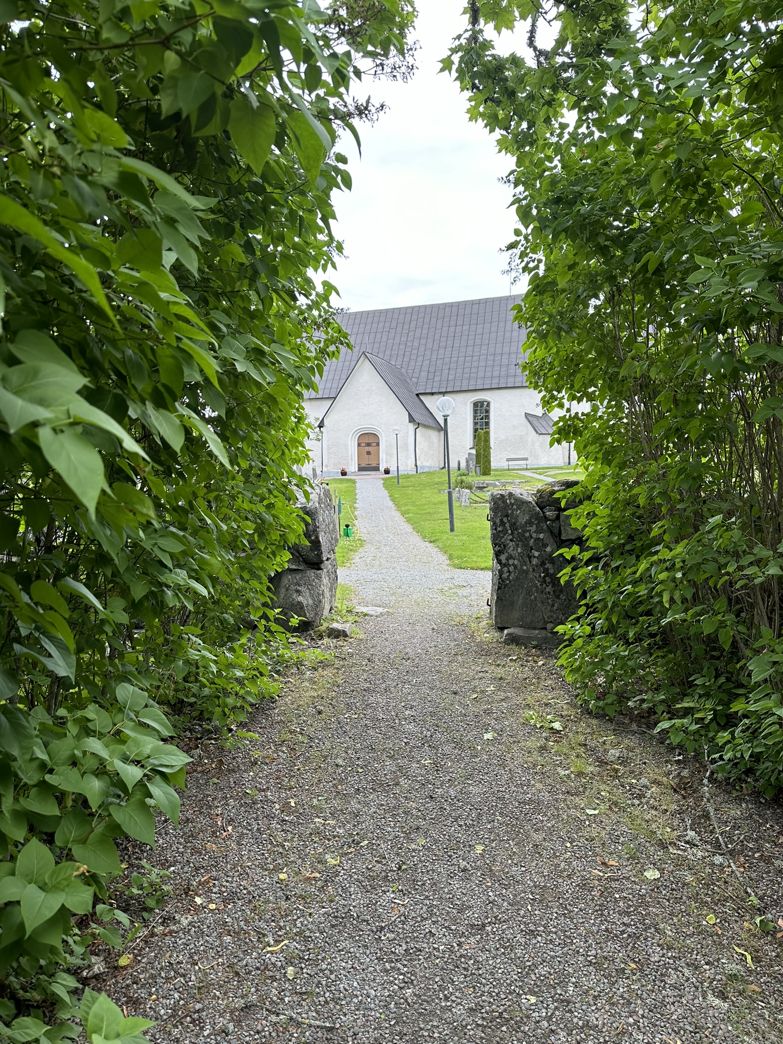 Mellan två gröna häckar leder en grusgång fram till Villberga kyrka.