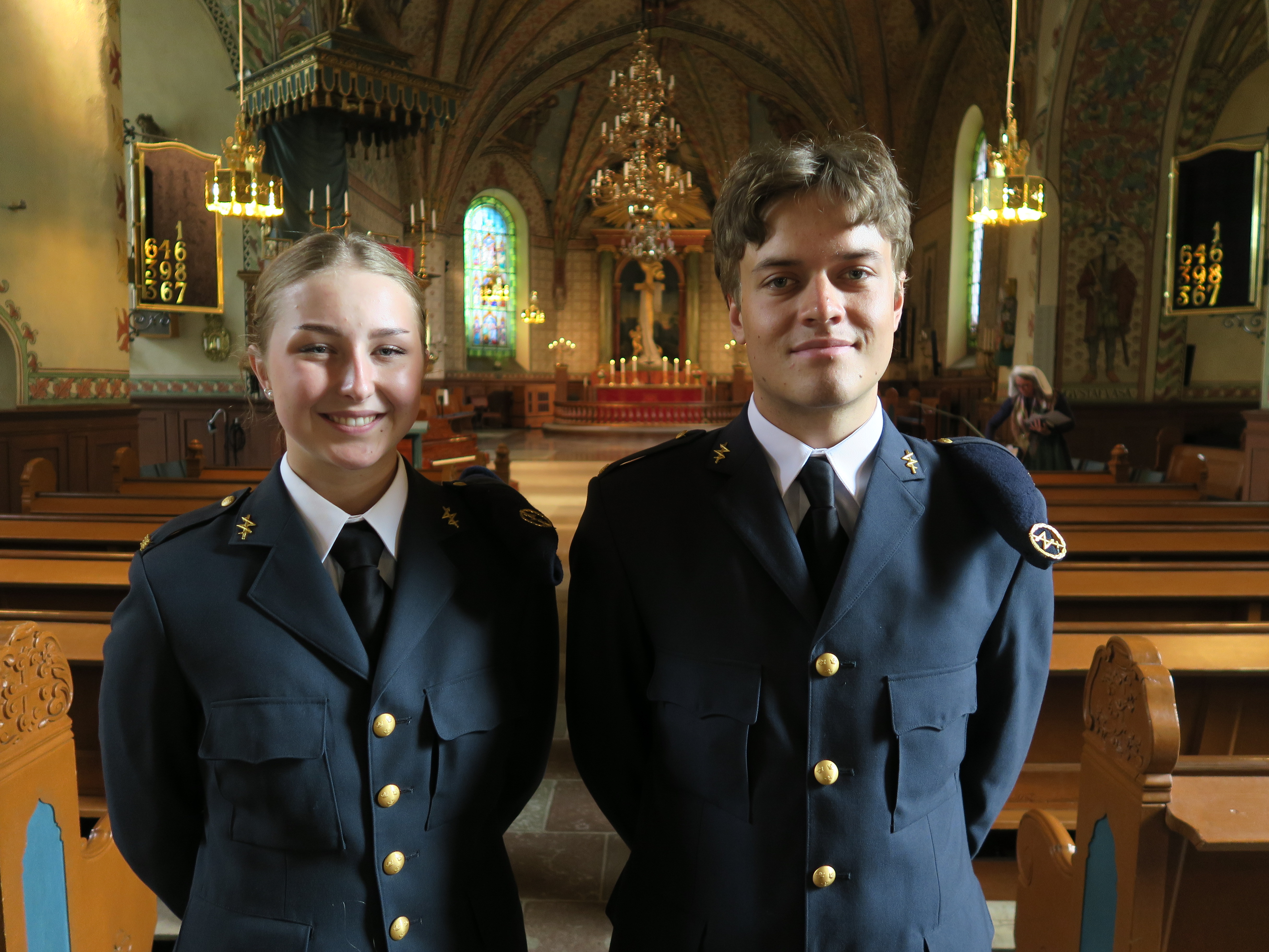 En kvinna och en man i militäruniformer står i en kyrka. De ler mot kameran.