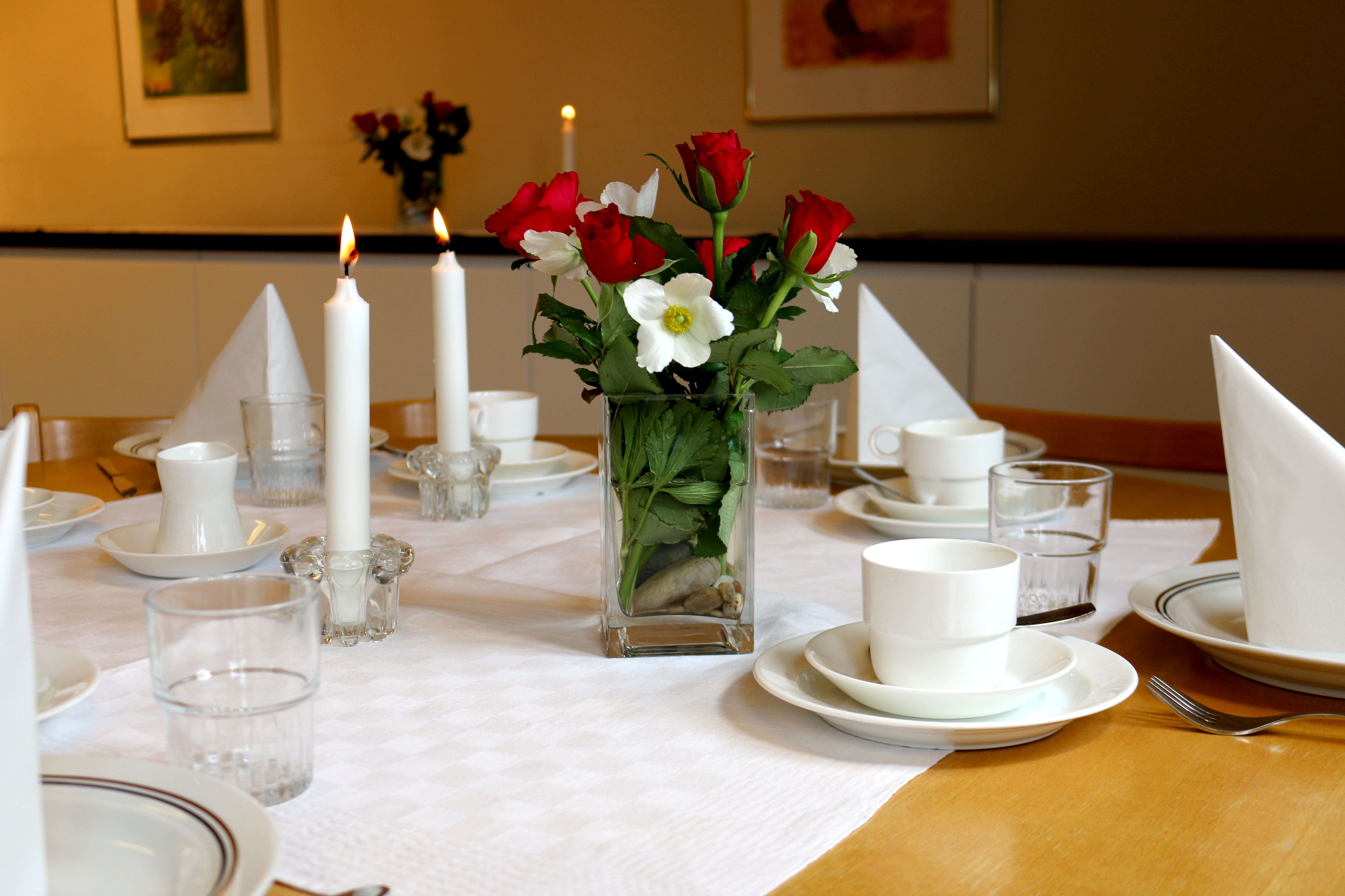 Dukat bord med ljus, kaffekoppar, servetter och blommor.