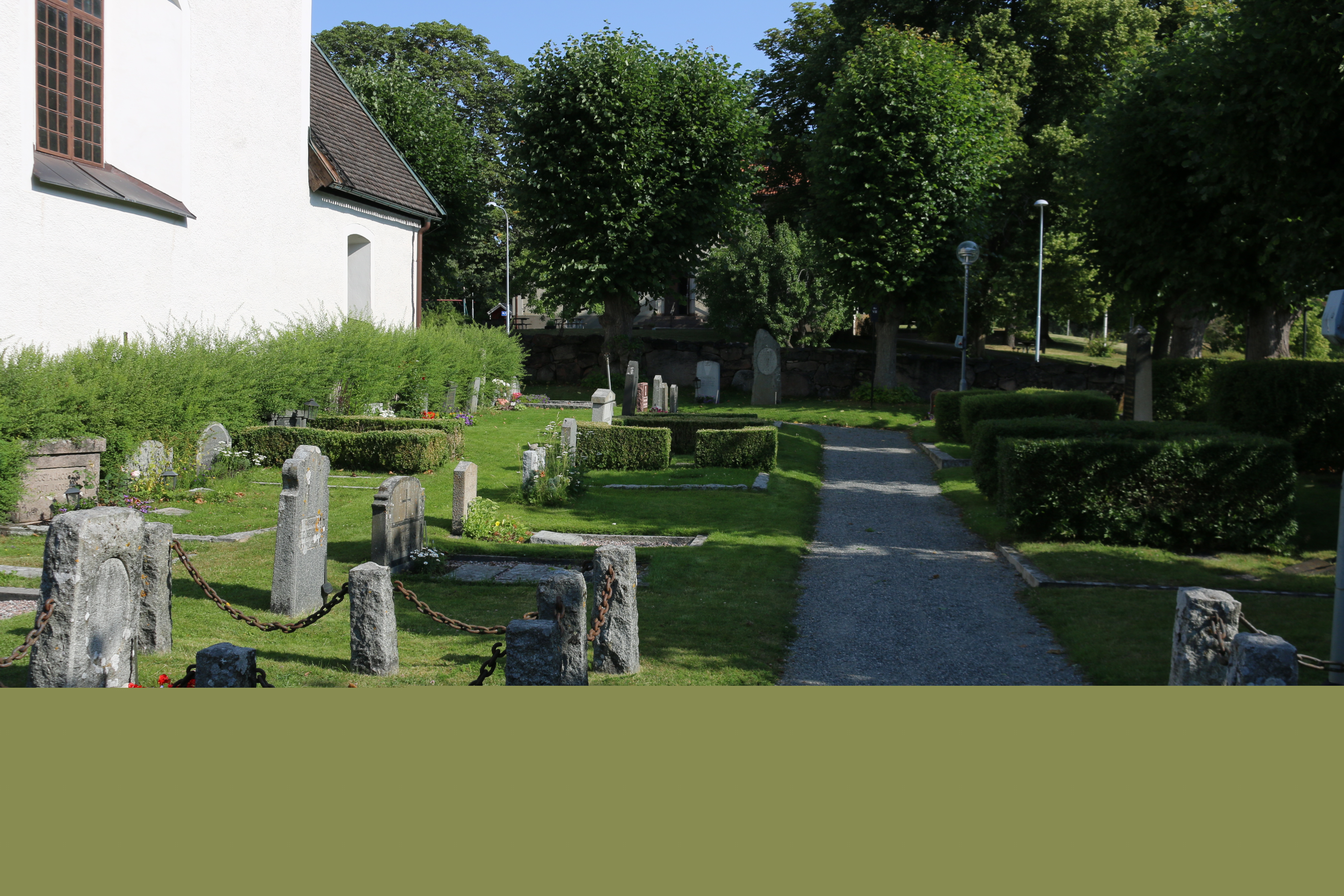 Del av Täby kyrkogård. Utöver gravar och grusgång syns lövverk, träd och en del av kyrkoväggen.