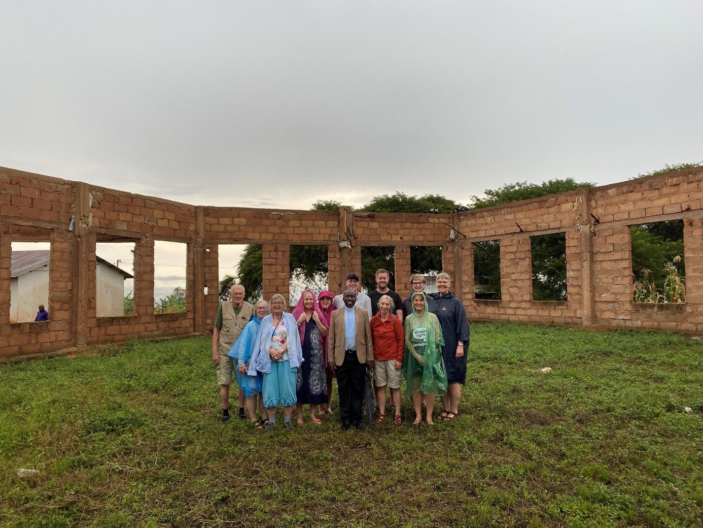 kyrka med tegelvägg  med gräs som golv och inget tak och fönster , män och kvinnor står och ler