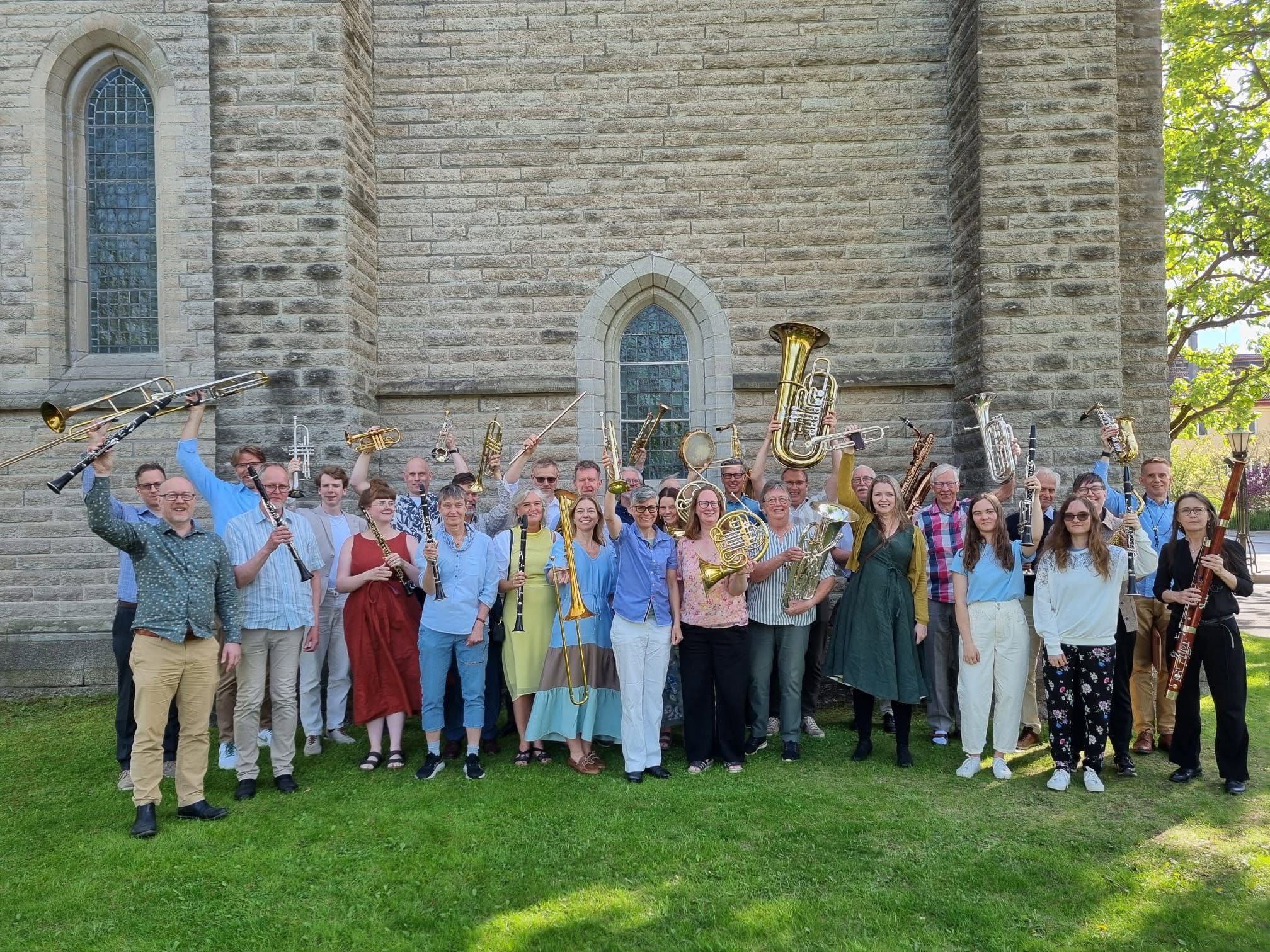 Olaus Petri Musikkår står utanför kyrkan och håller upp sina instrument