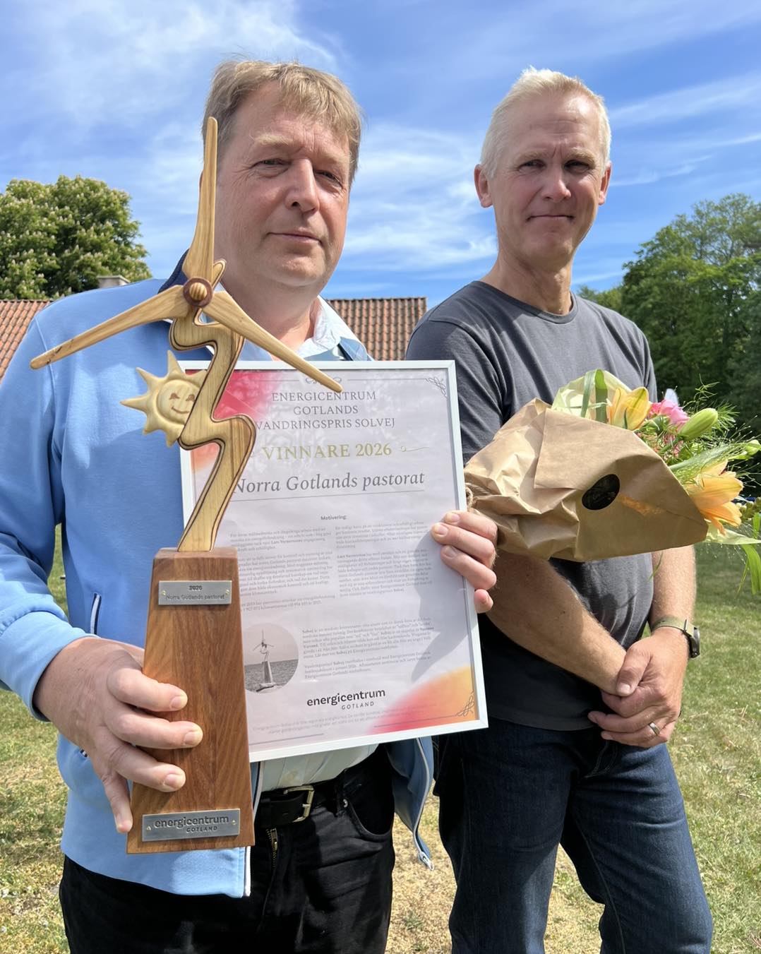 Lars Vernersson står med träskulpturen Solvej i handen, och ett diplom med prismotivering. Han har också en blombukett. Patrick Dahl från Energicentrum flankerar.