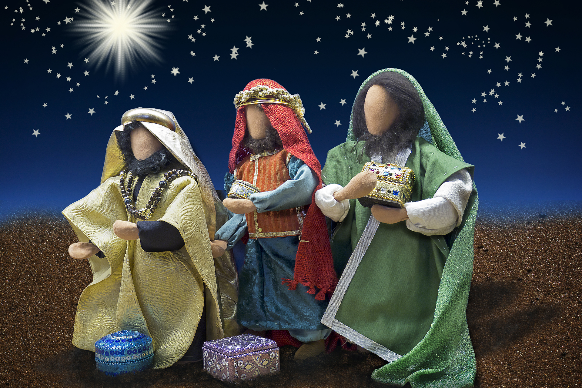 Tre tygdockor i färgglada kläder, föreställande de tre vise männen. Mot mörk blå bakgrund och en framträdande stjärna.