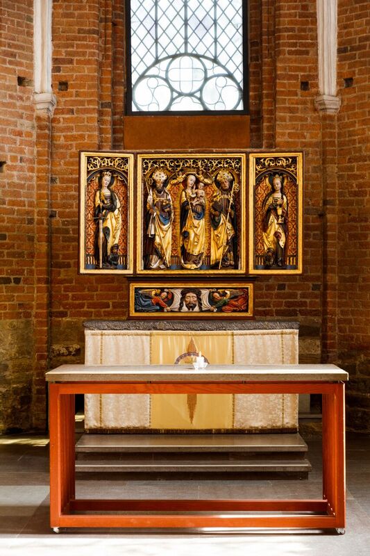 Klosterkyrkans altartavla och ett portabelt altare i trä med stenskiva. På det bortabla altaret står en ljusstake med ett tänd ljus. 