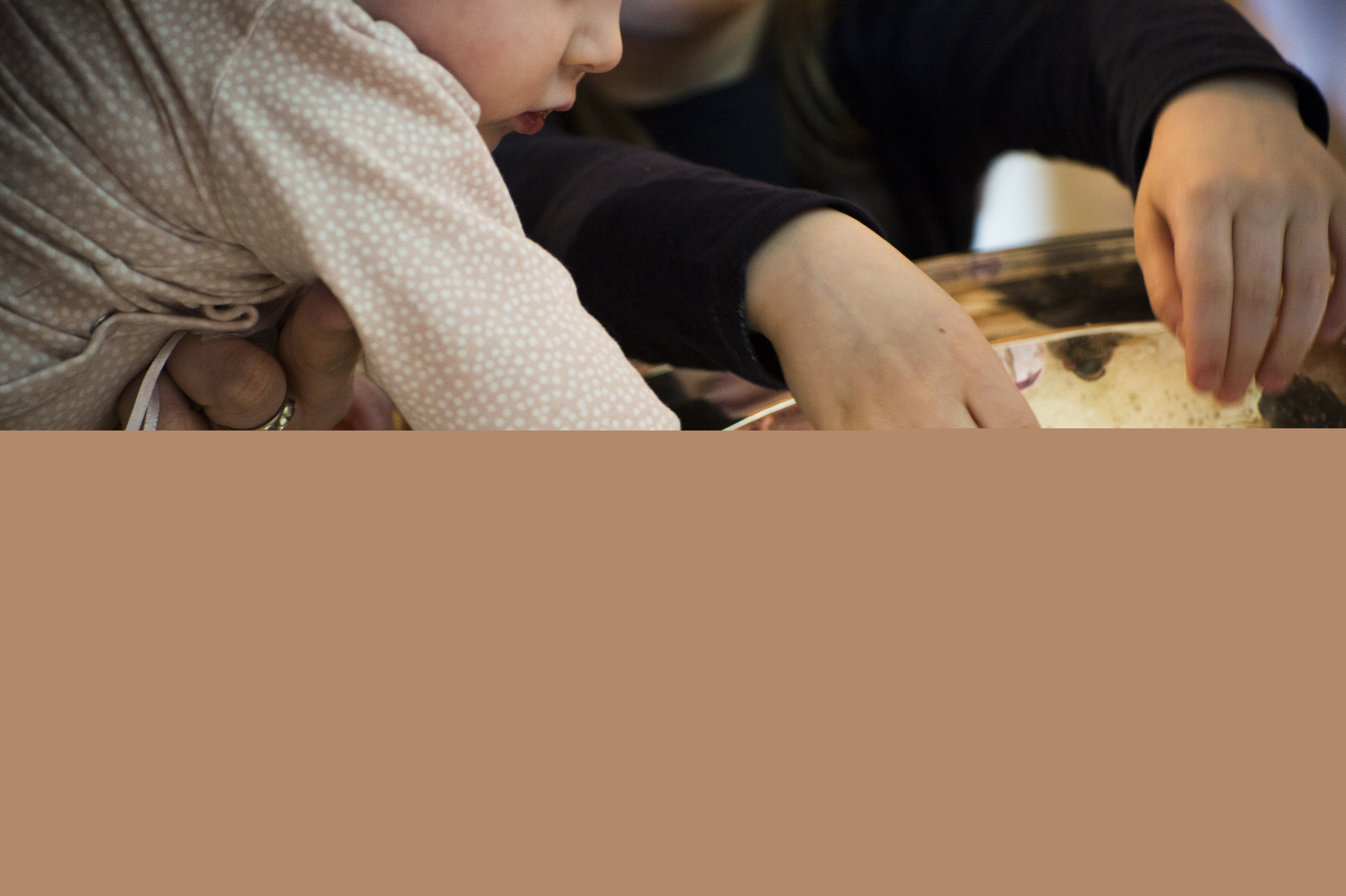 Närbild på dopfunt med barnhänder som rör vid vattnet i dopskålen