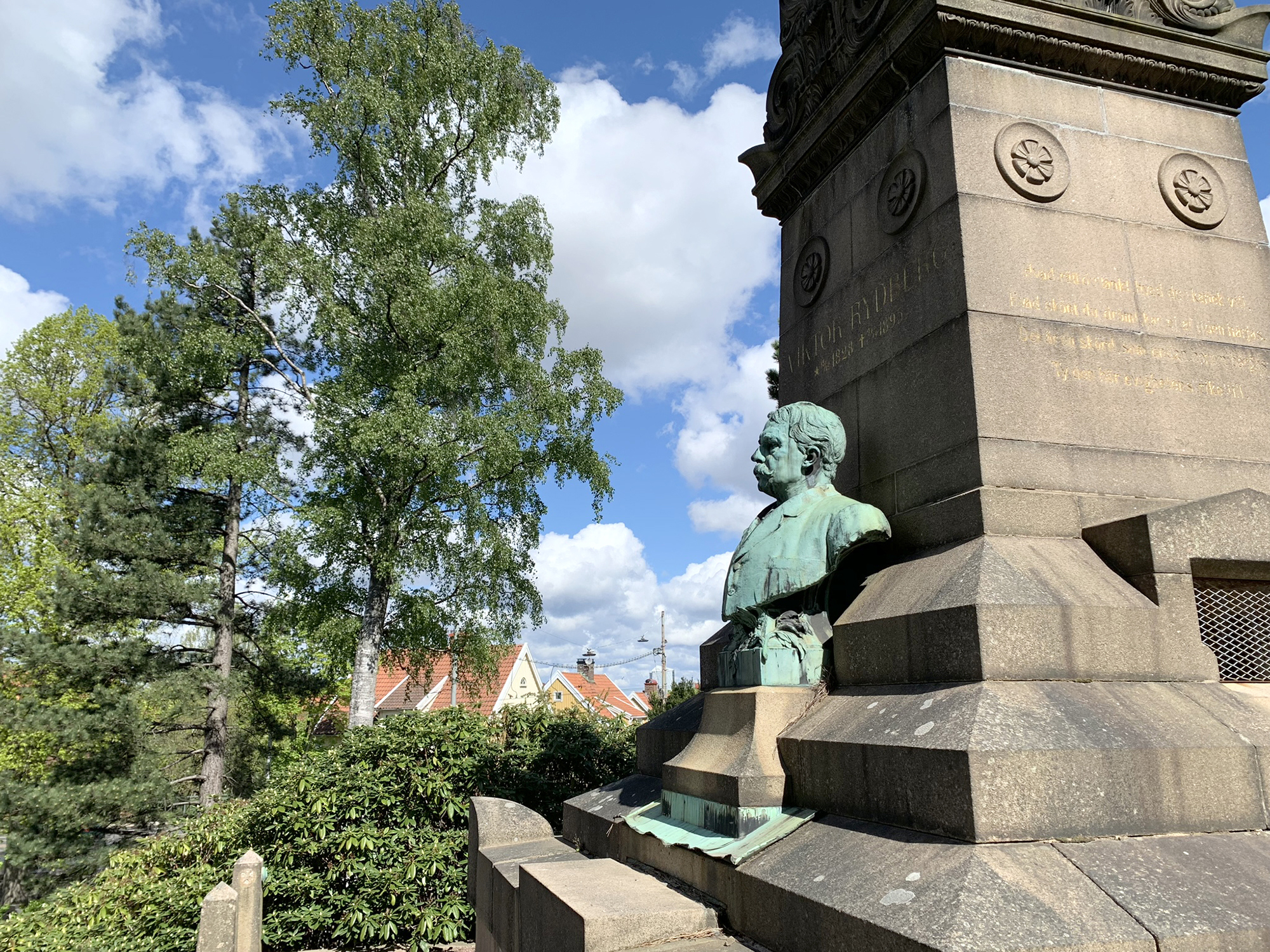 Viktor Rydbergs gravplats på Östra kyrkogården med Viktor i profil i förgrund och bostadshus i bakgrund.