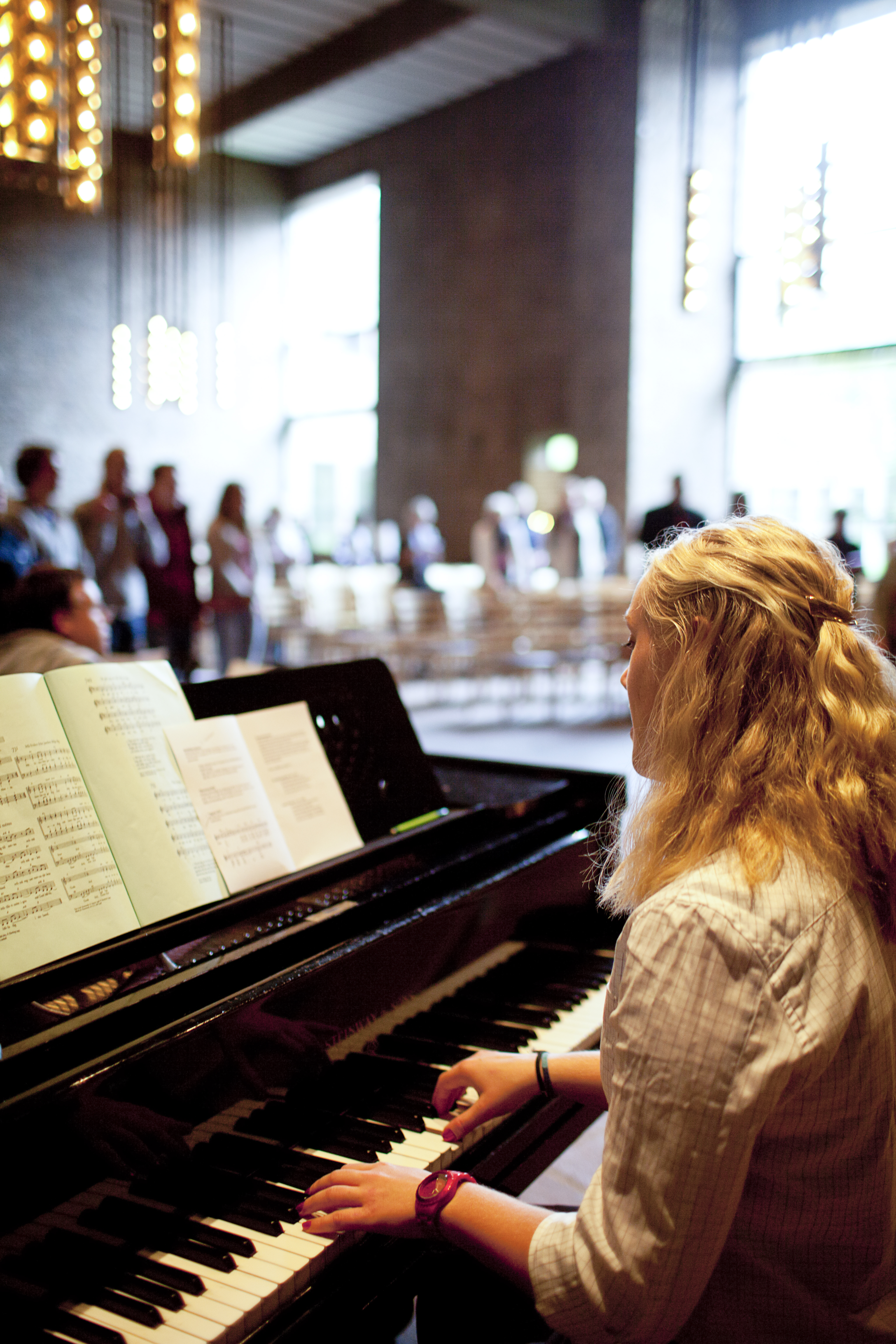 En blond kvinna spelar piano för en liten publik.