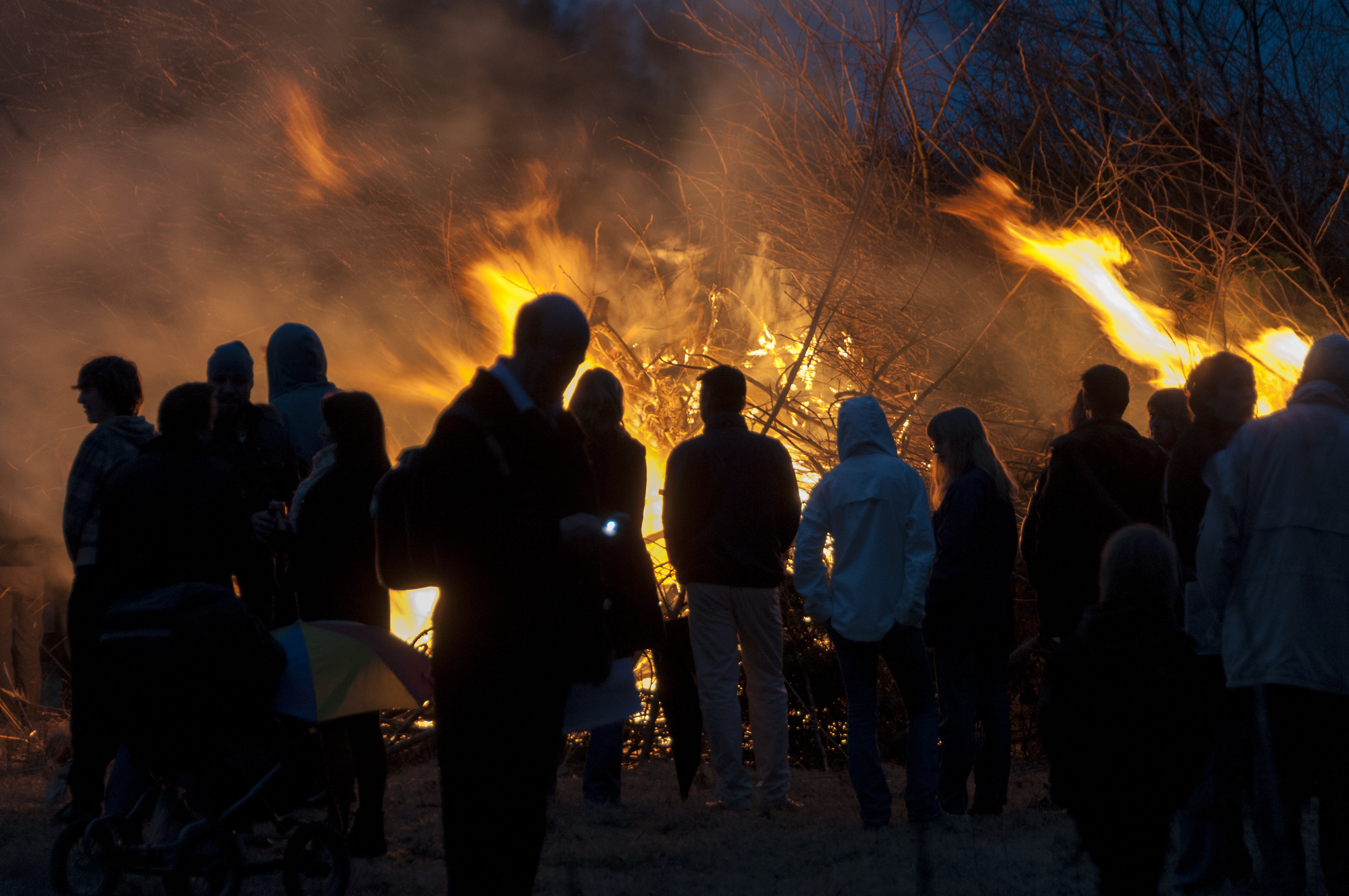 En grupp människor står vid en majbrasa i mörkret.