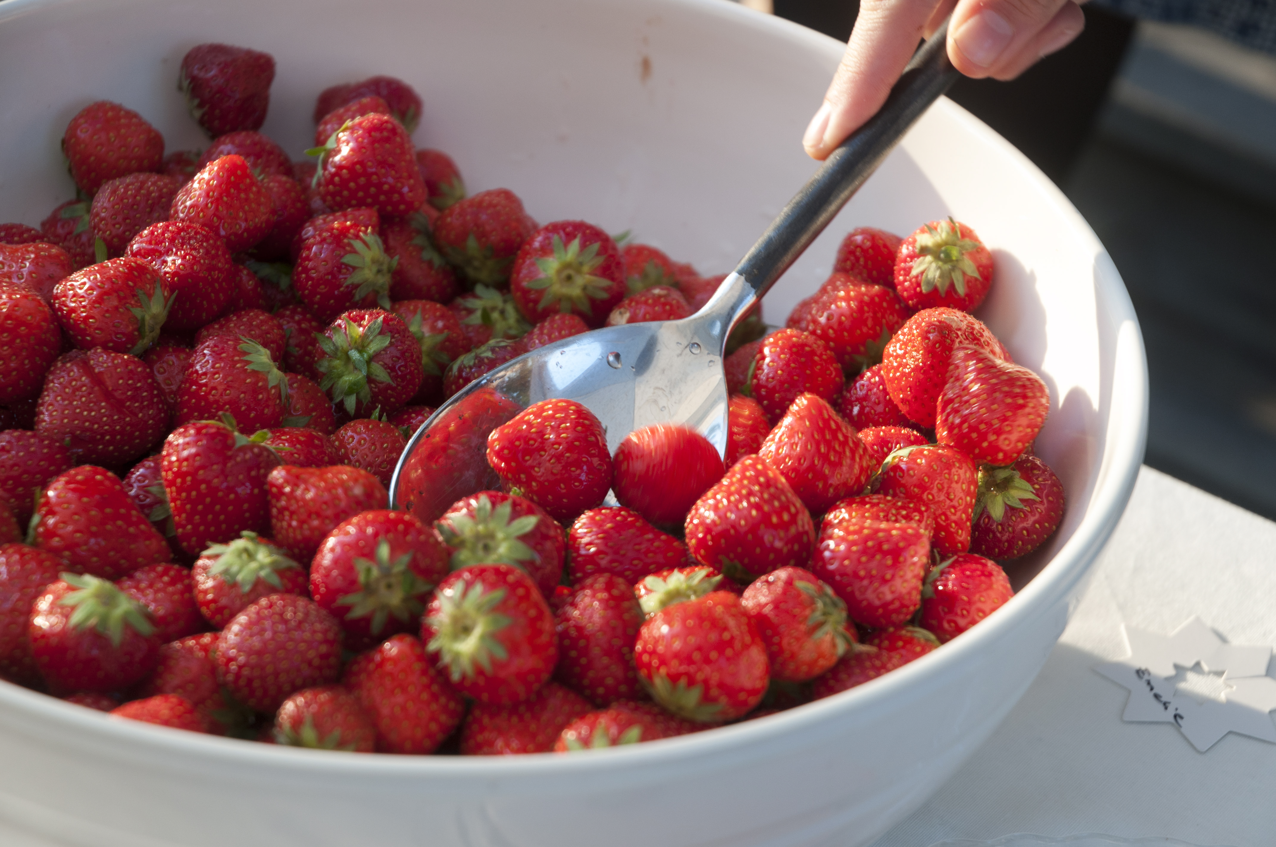 Någon tar jordgubbar ur en stor skål.