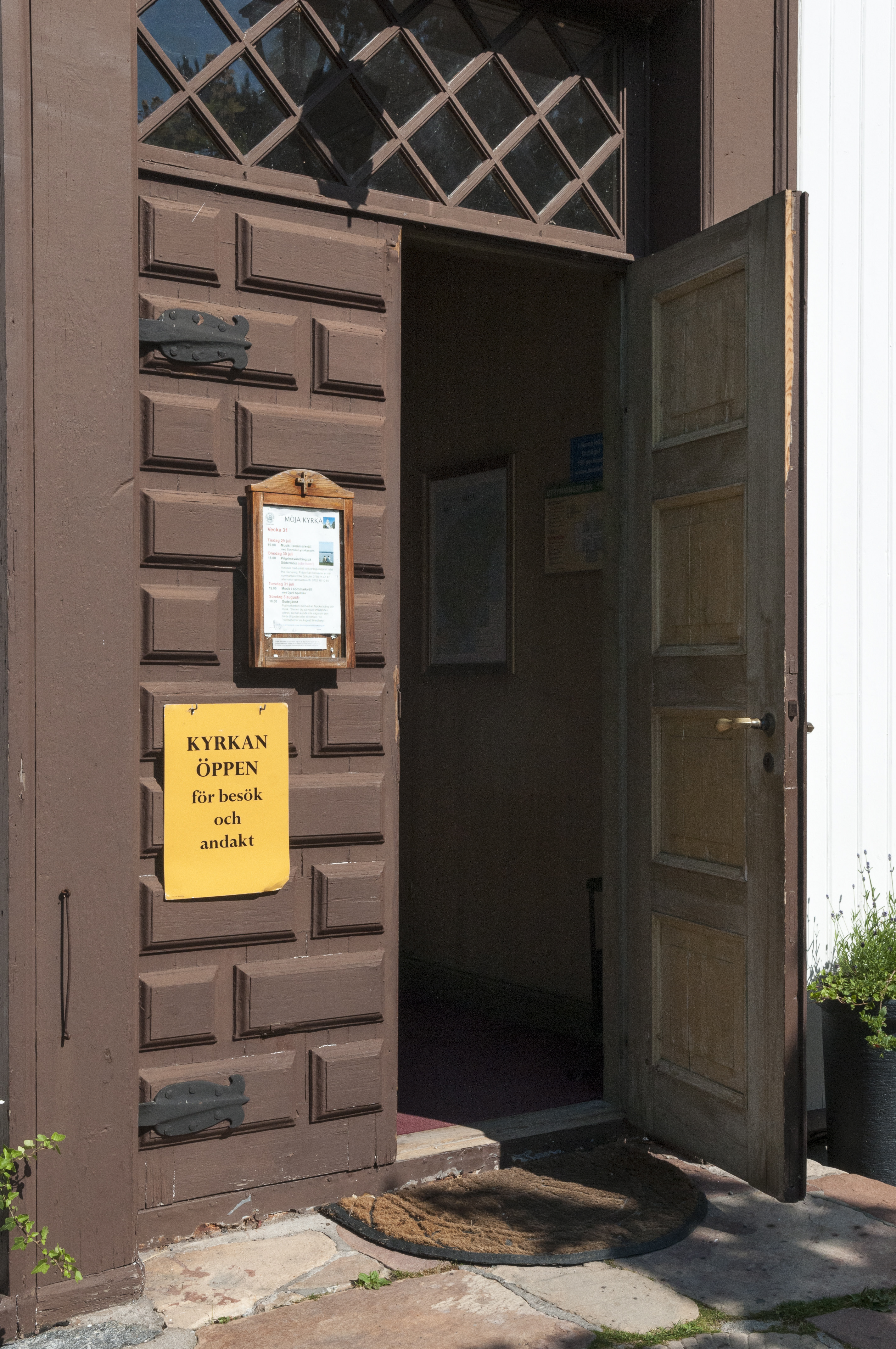 En lapp på en öppen dörr med texten Kyrkan är öppen för besök och andakt.