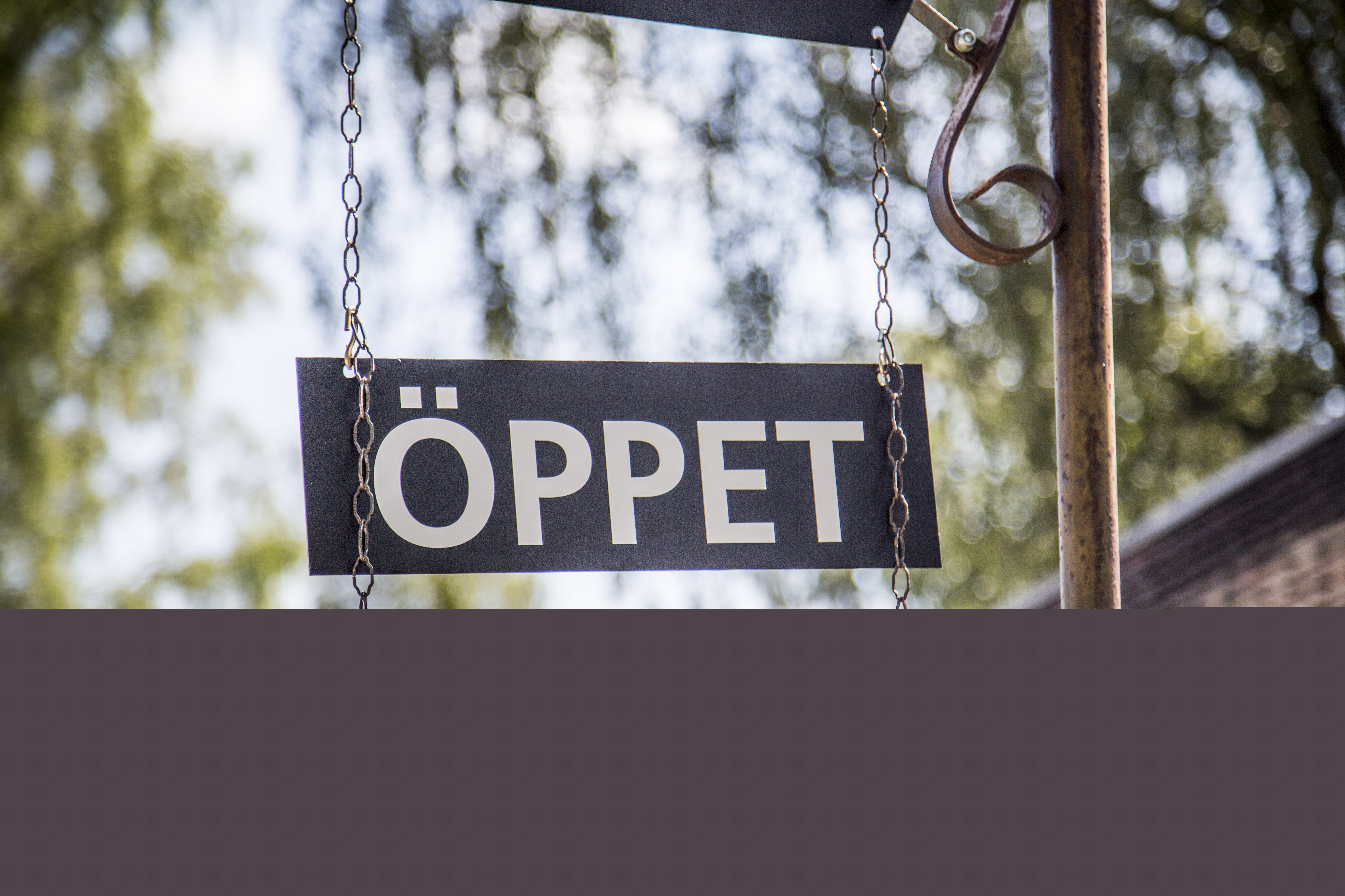 En skylt med texten Öppet hänger på en stolpe utomhus.