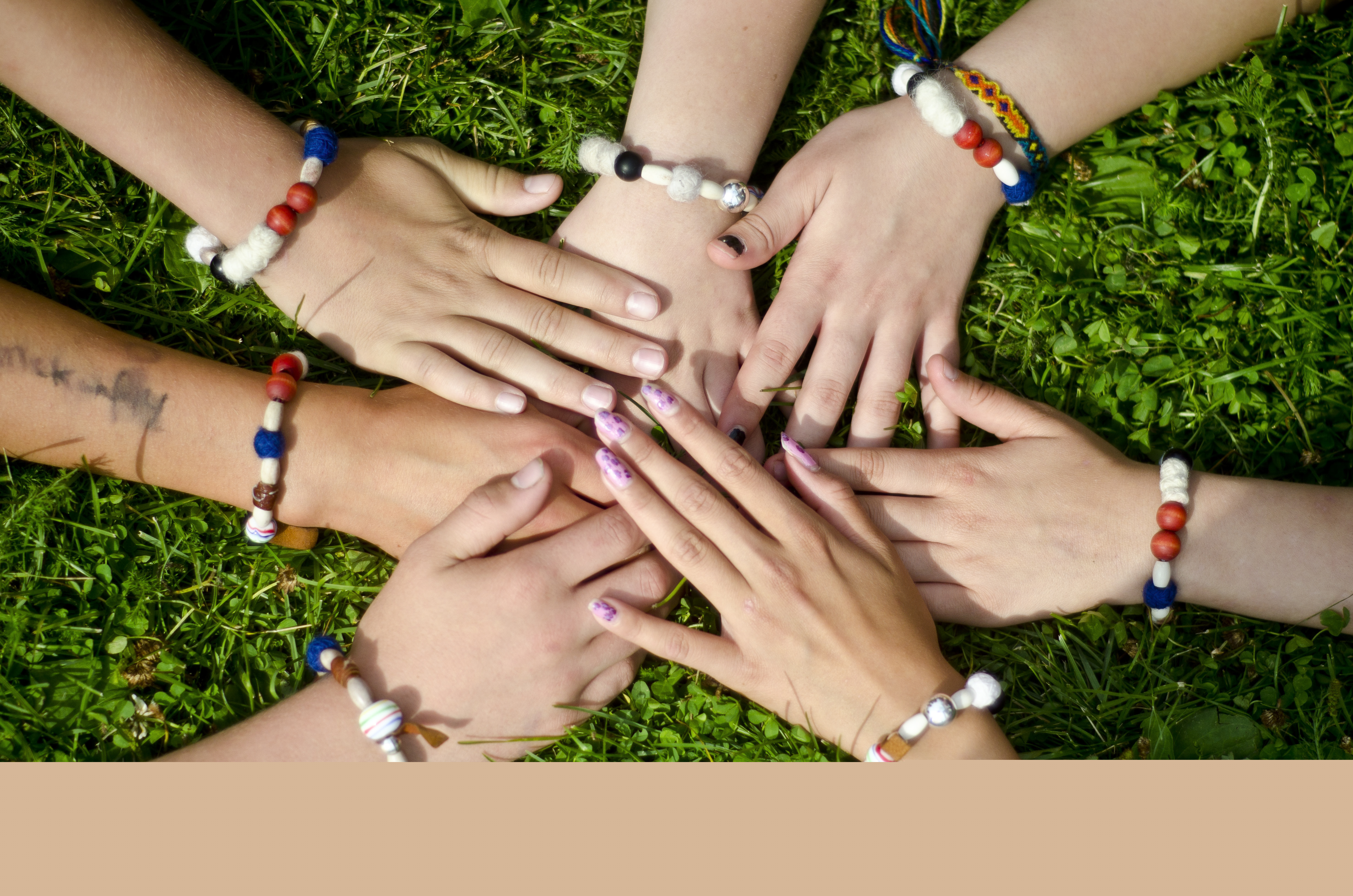 Några personer med varsitt pärlarmband lägger sina händer på varandra i gräset.