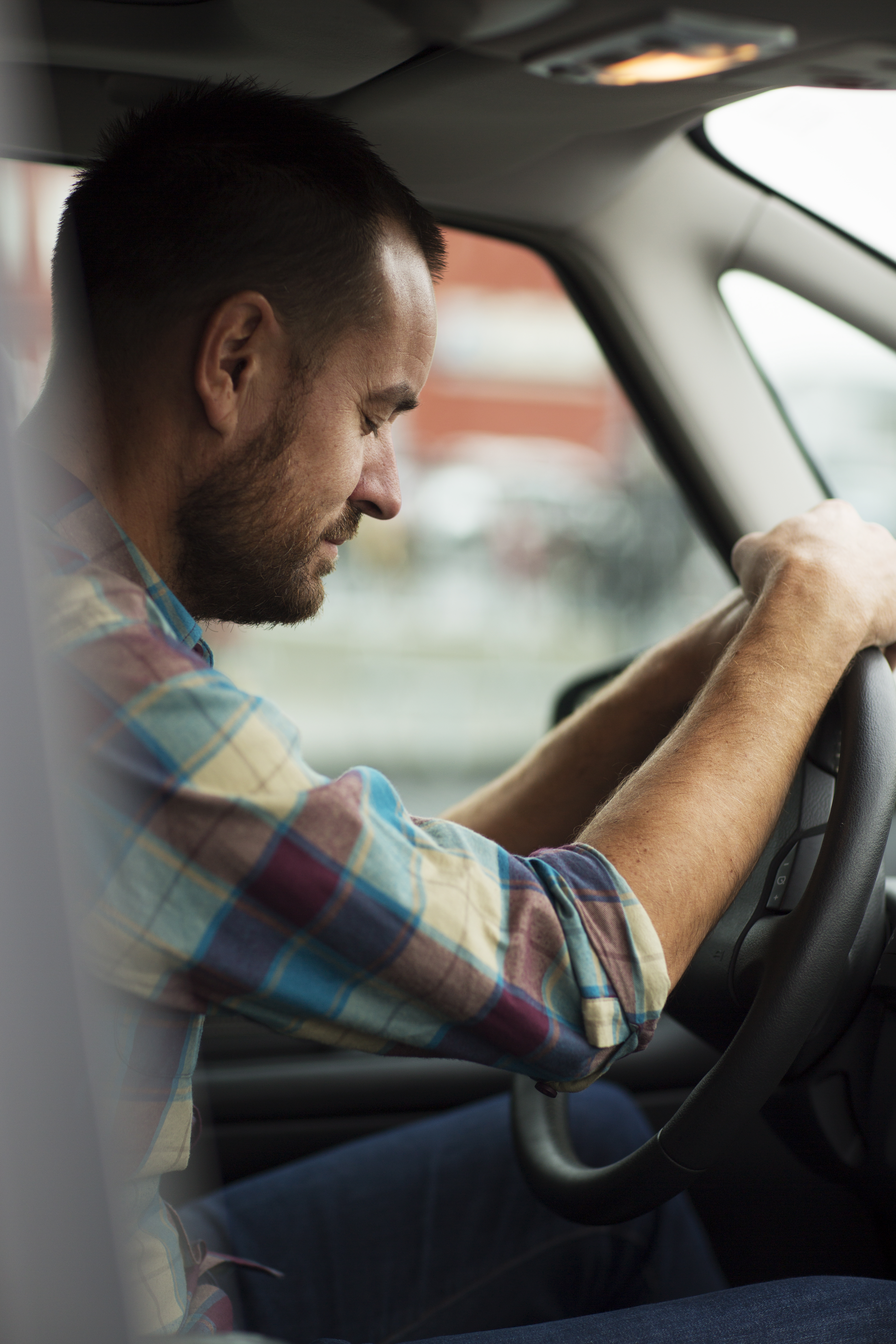 En man sitter i en bil med händerna på ratten och blundar.