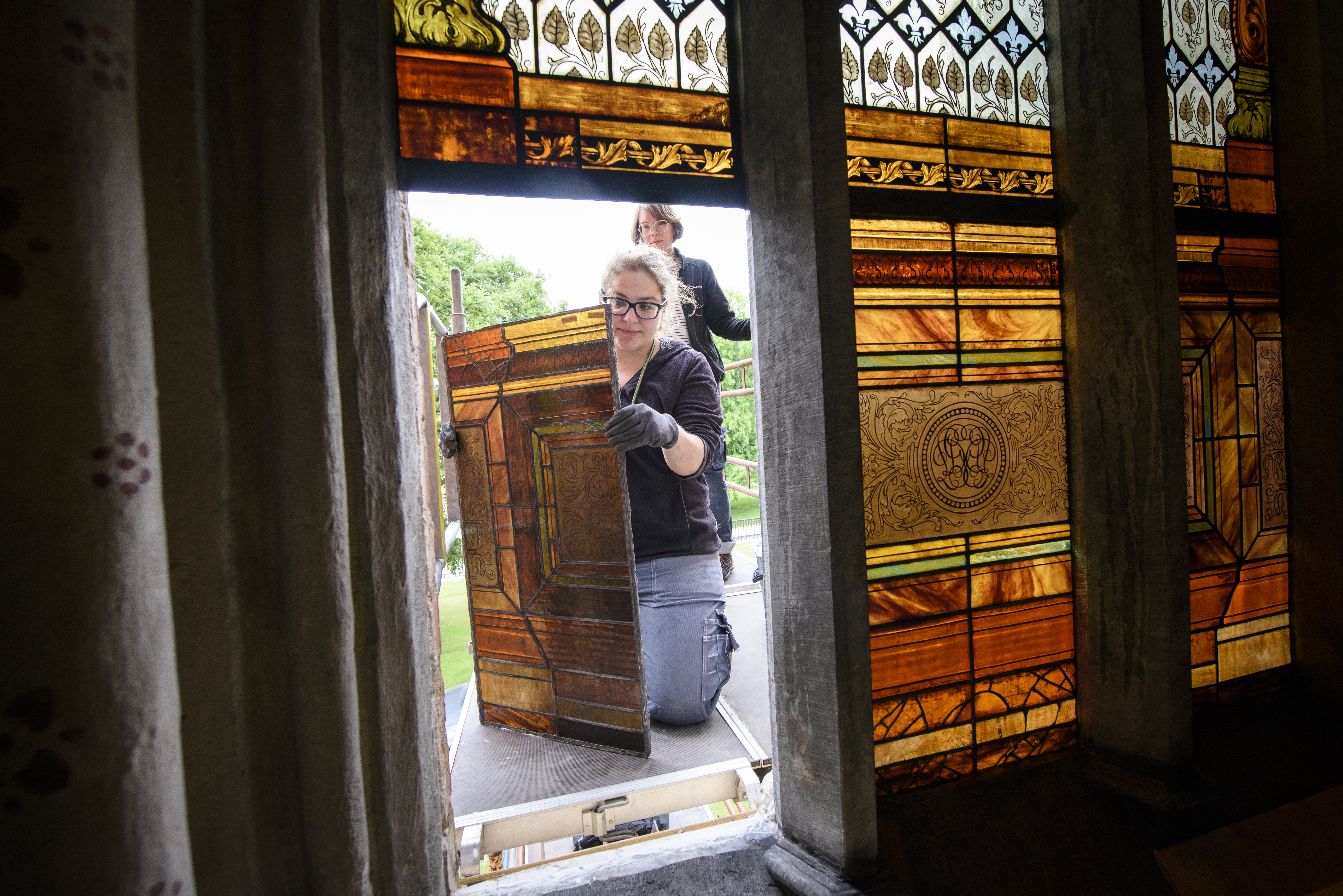 Två arbetare renoverar ett färggrant kyrkfönster.