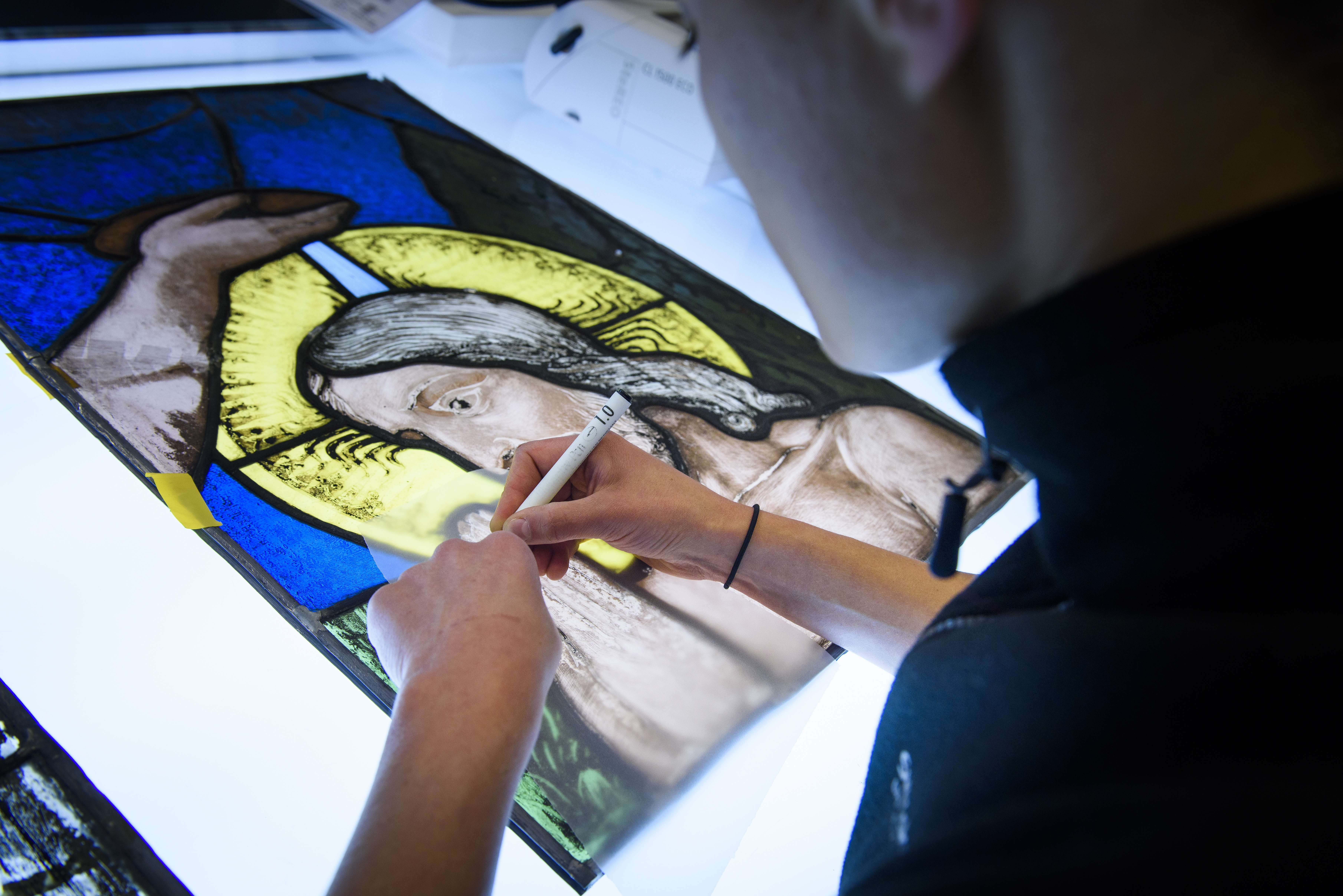 En konservator sitter vid ett bord och handmålar på ett kyrkfönster.