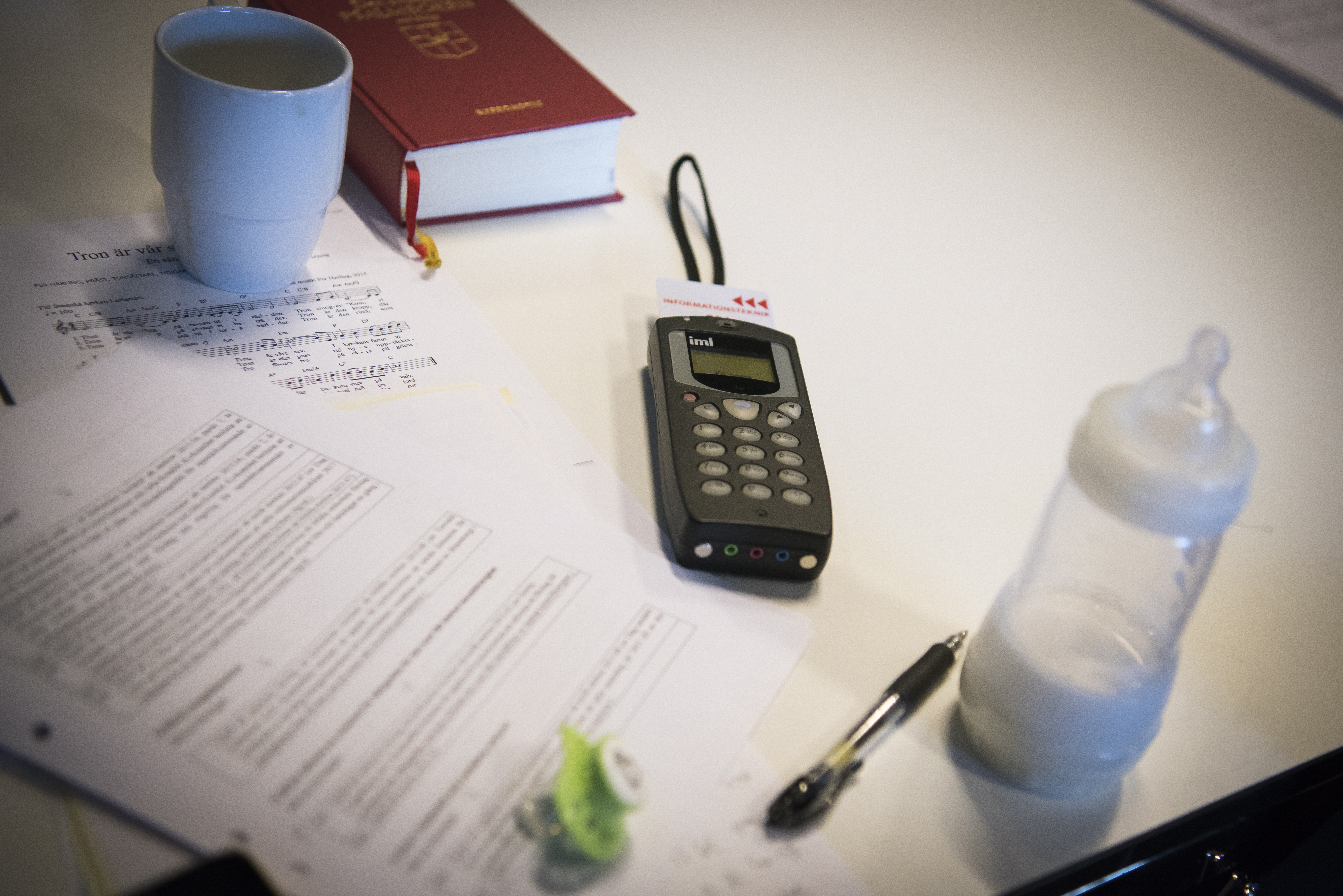 Ett bord med en napp, en nappflaska, en mobiltelefon, en bibel och några papper.