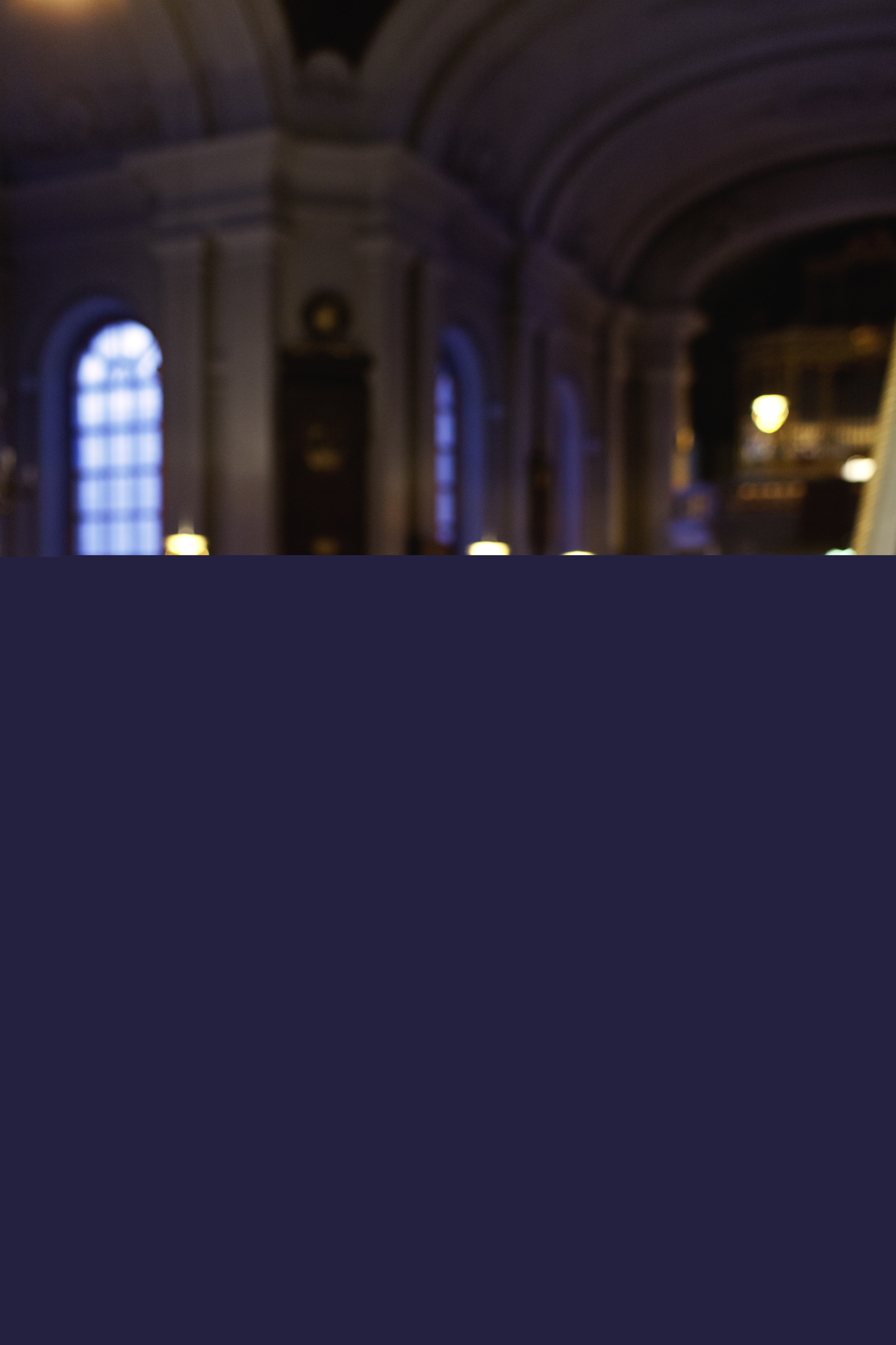 Ett sånghäfte och en triangel ligger på ett notställ. Fullsatta kyrkbänkar i bakgrunden.