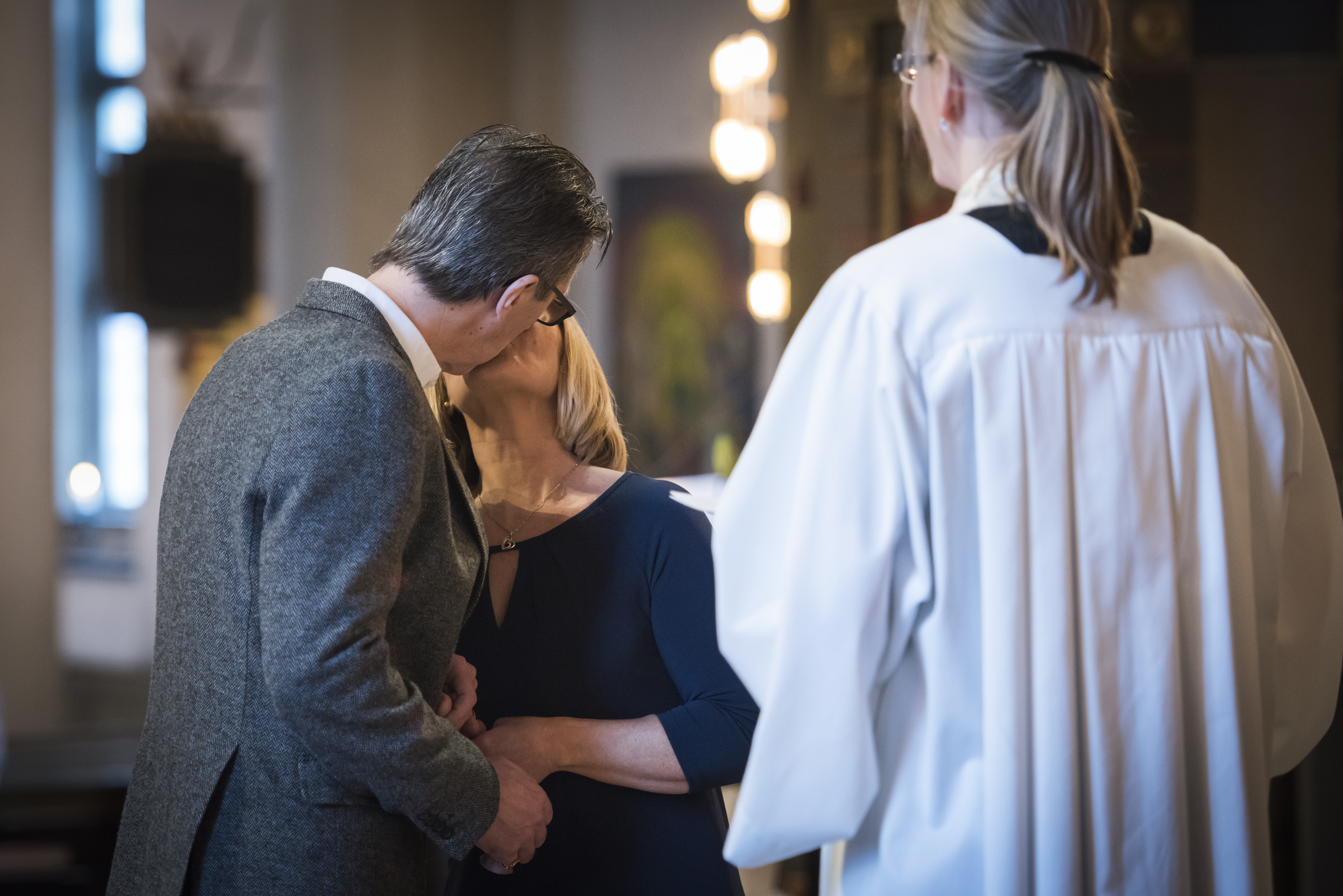 Ett brudpar kysser varandra. En kvinnlig präst står framför.