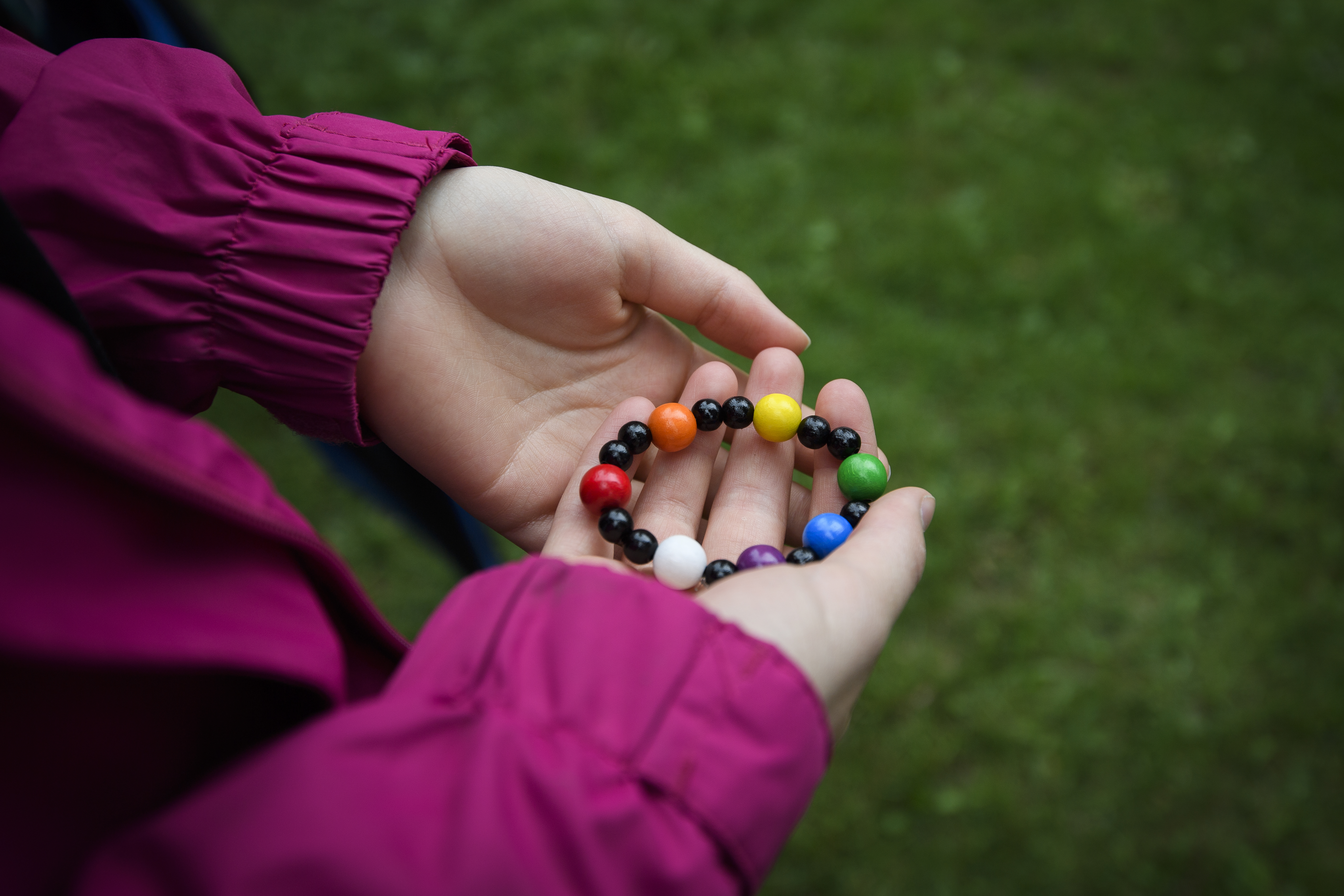 En person håller i ett pärlarmband med pärlor i olika färger och former.