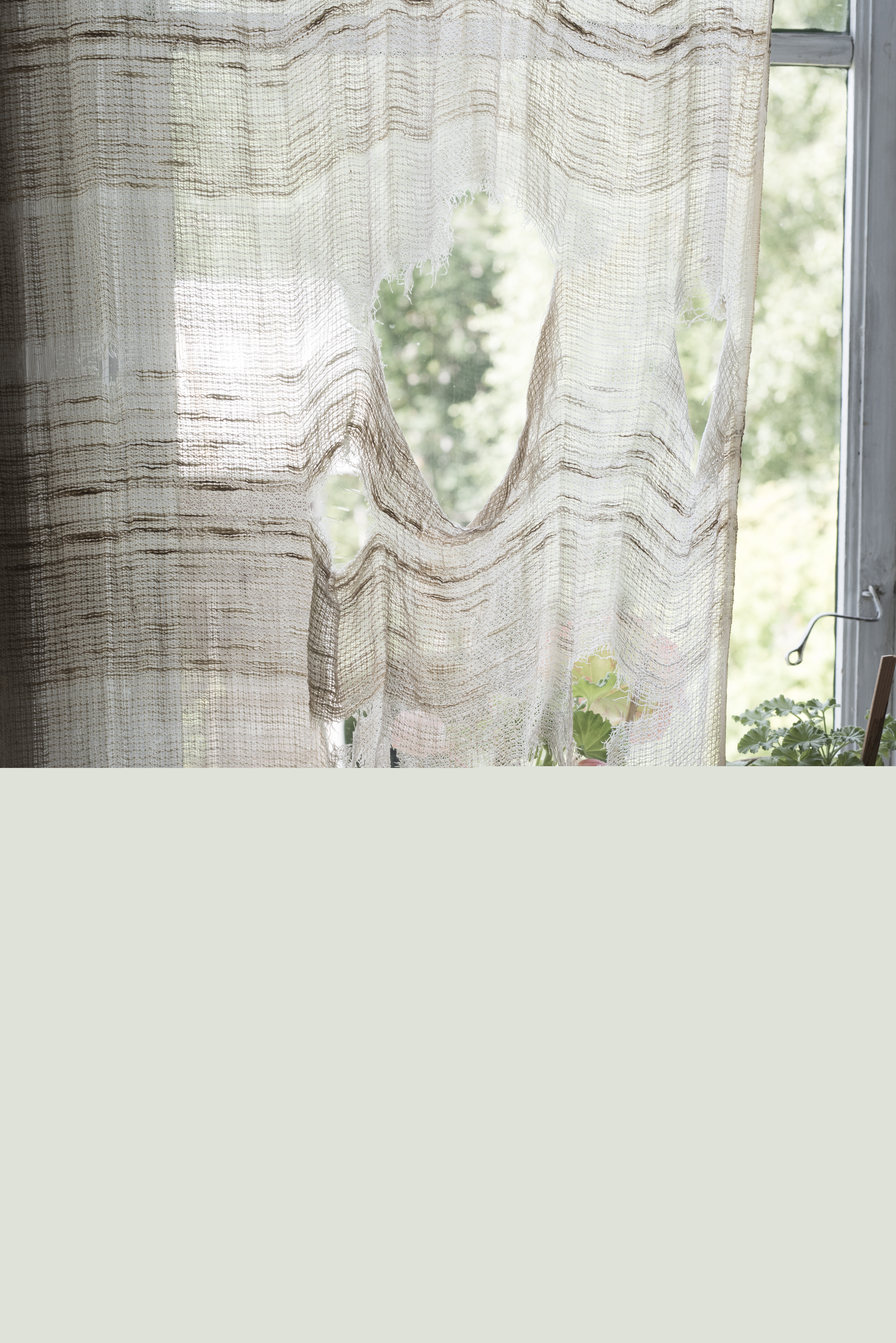En gammal trasig gardin hänger i ett fönster.