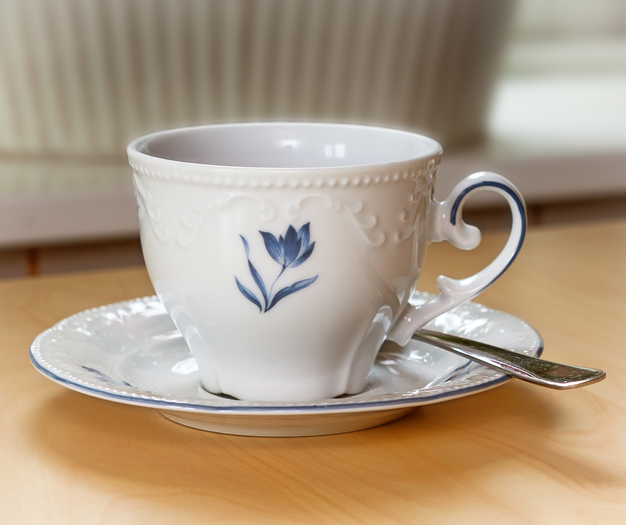 Närbild på en vit kaffekopp med en blå målad blomma.