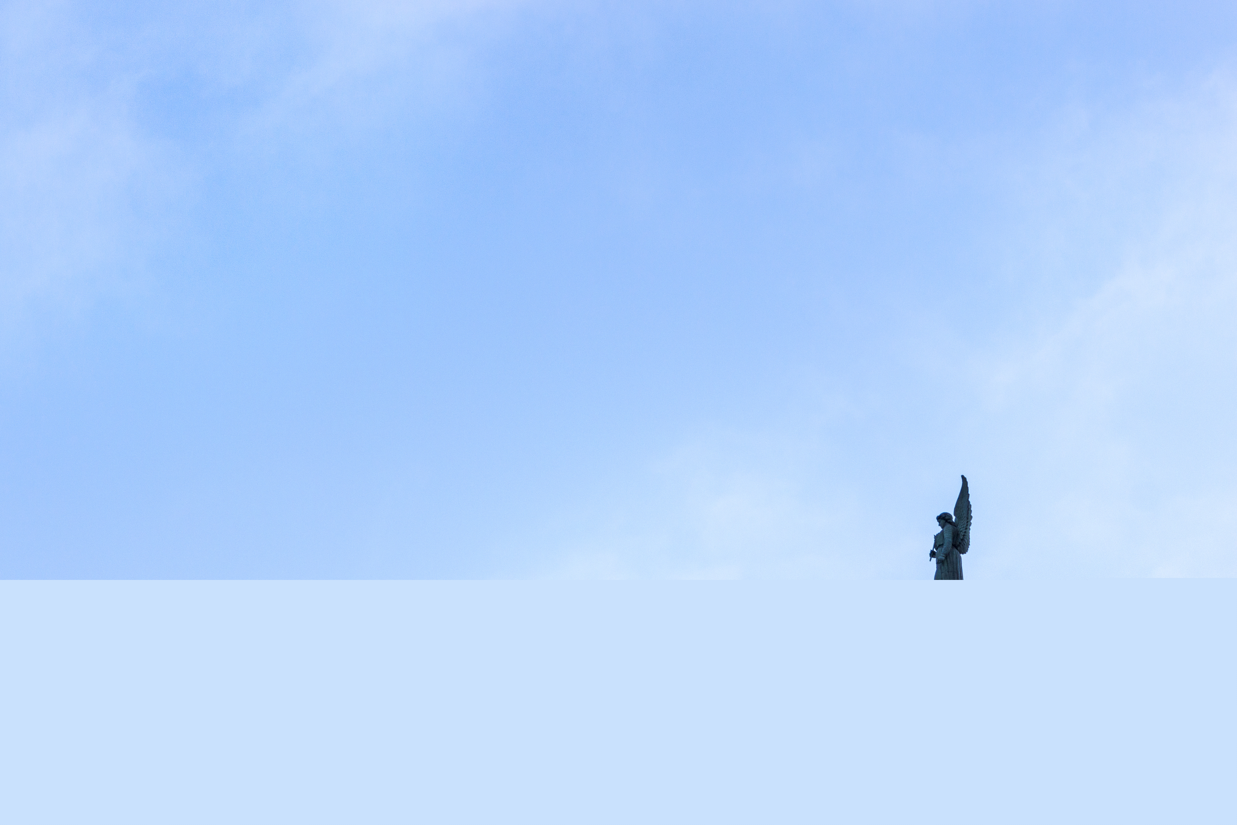 En änglastaty på ett tak mot blå himmel.