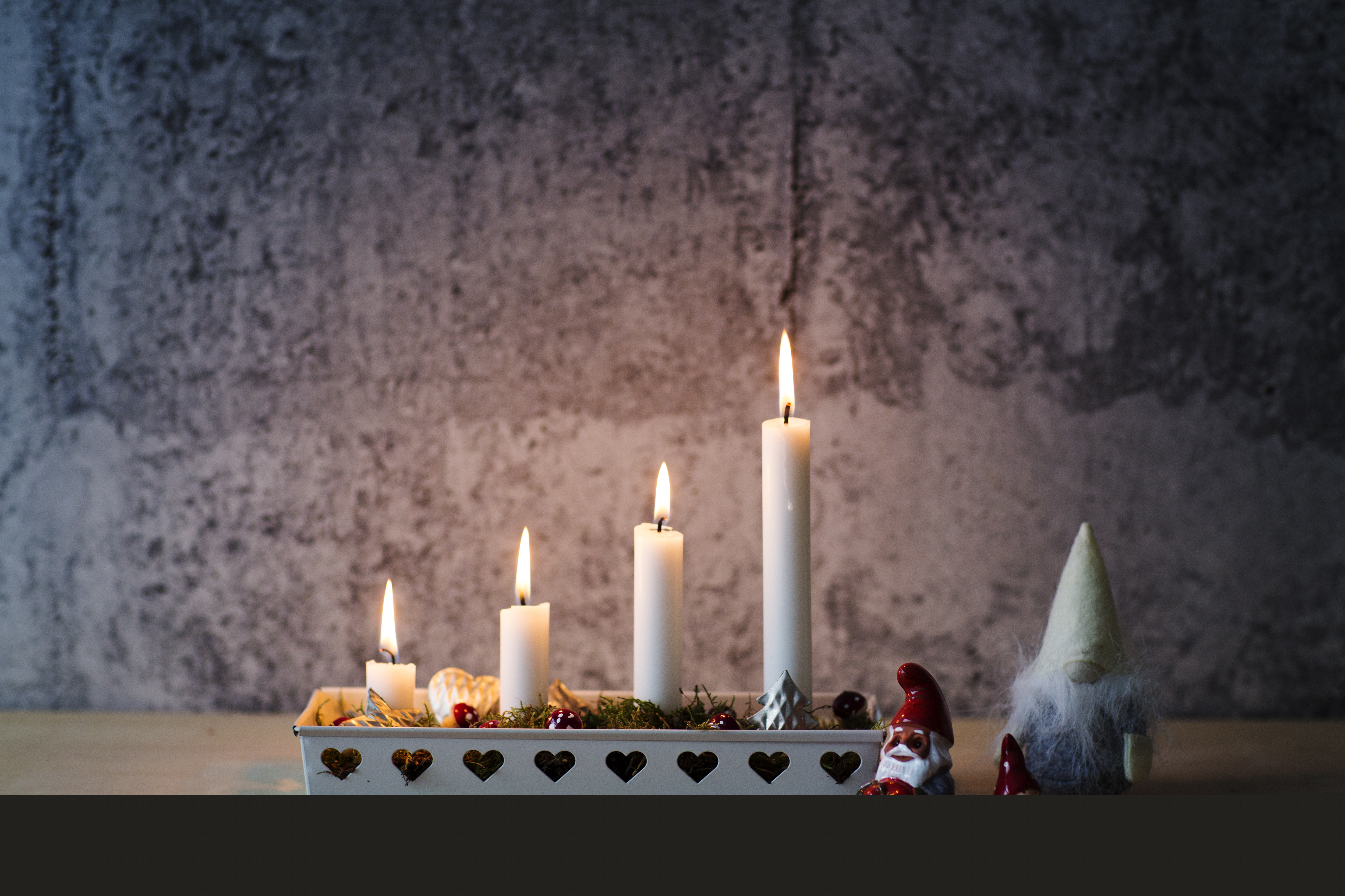 En adventsljusstake med fyra ljus tända. Några små tomtar står bredvid.