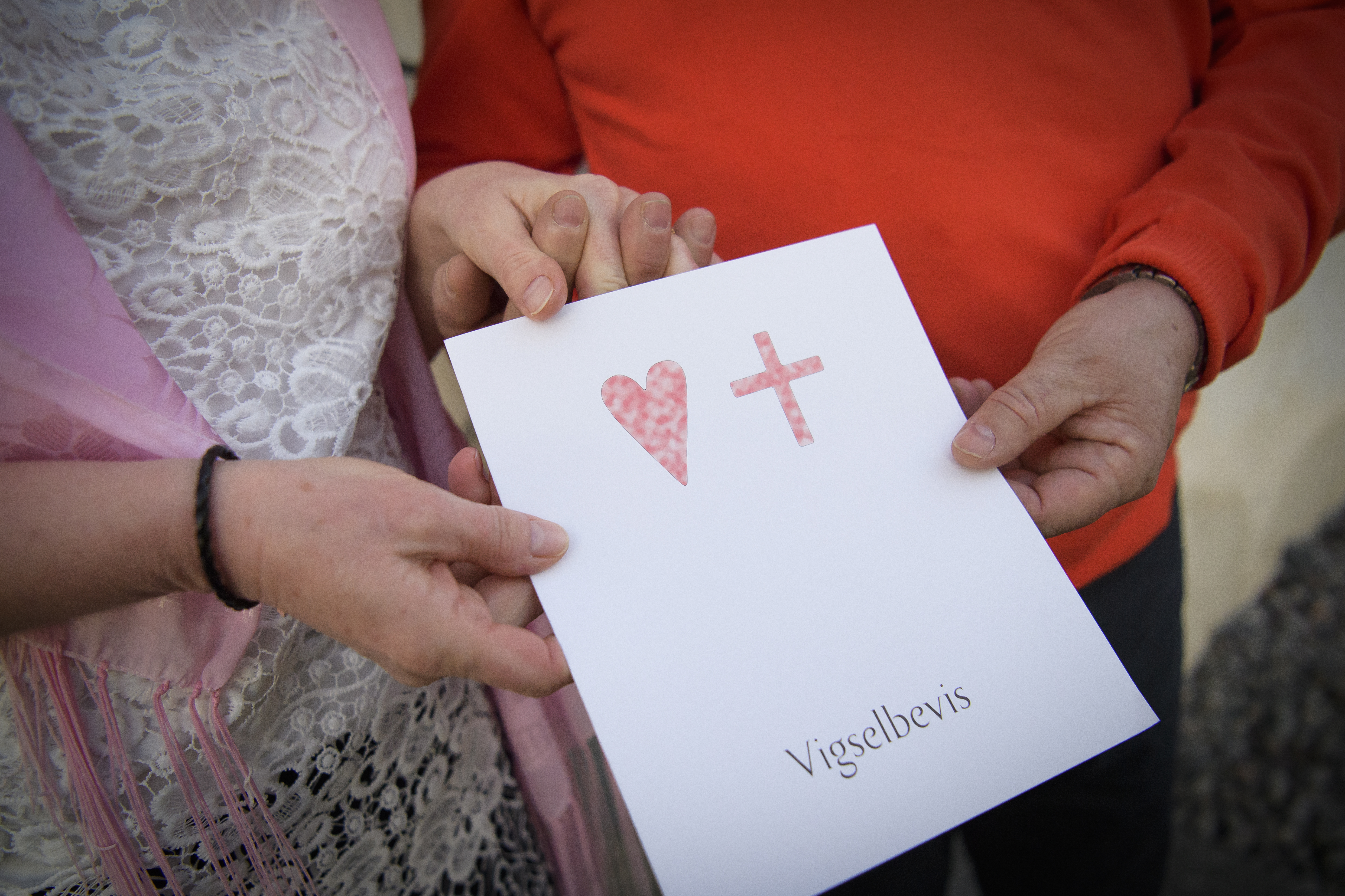 En man och en kvinna håller i ett papper med ett hjärta, ett kors och texten Vigselbevis.