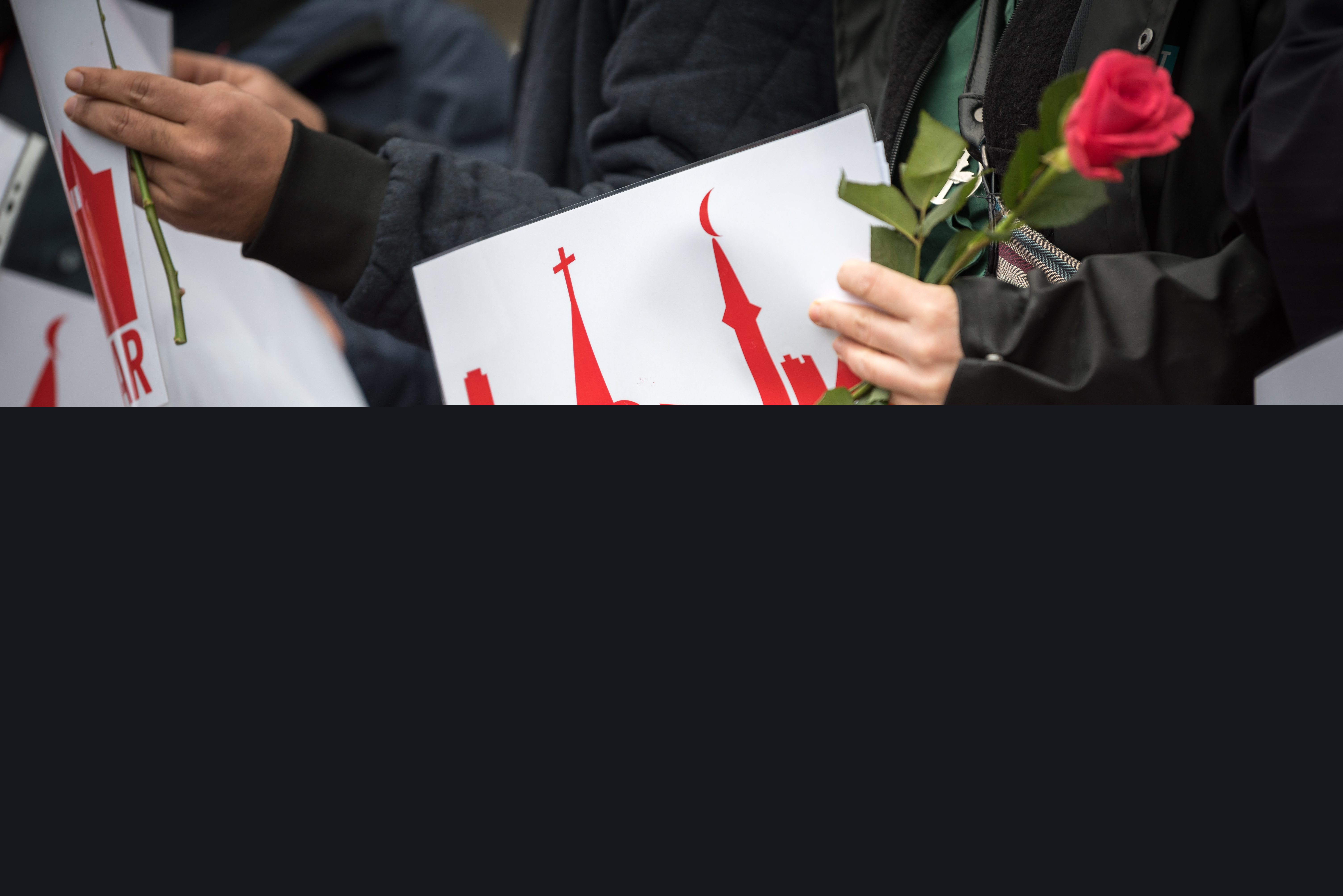 Några människor står med röda rosor och skyltar med texten Goda grannar.