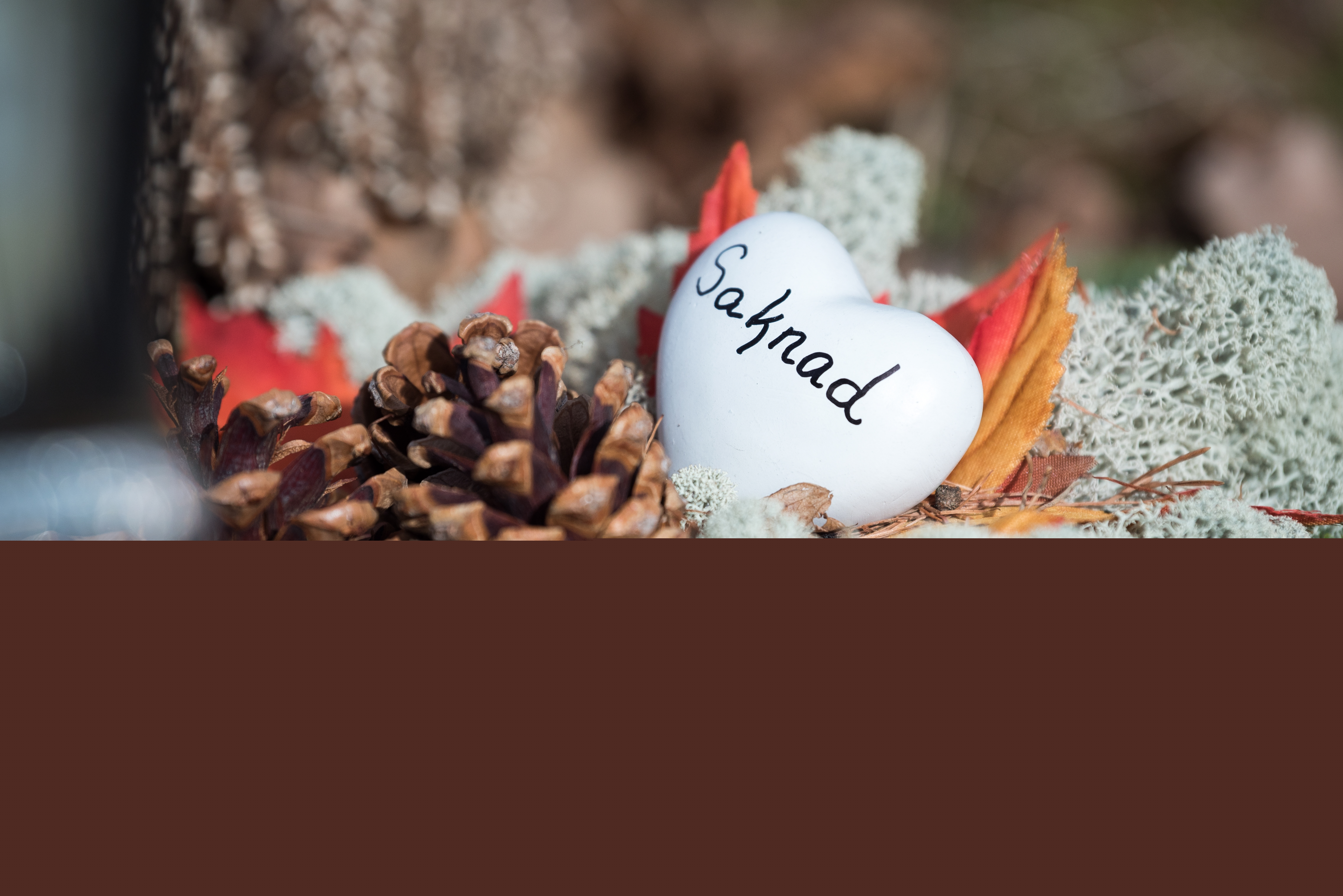 Närbild på ett litet hjärta med texten Saknad som ligger på en gravkrans.