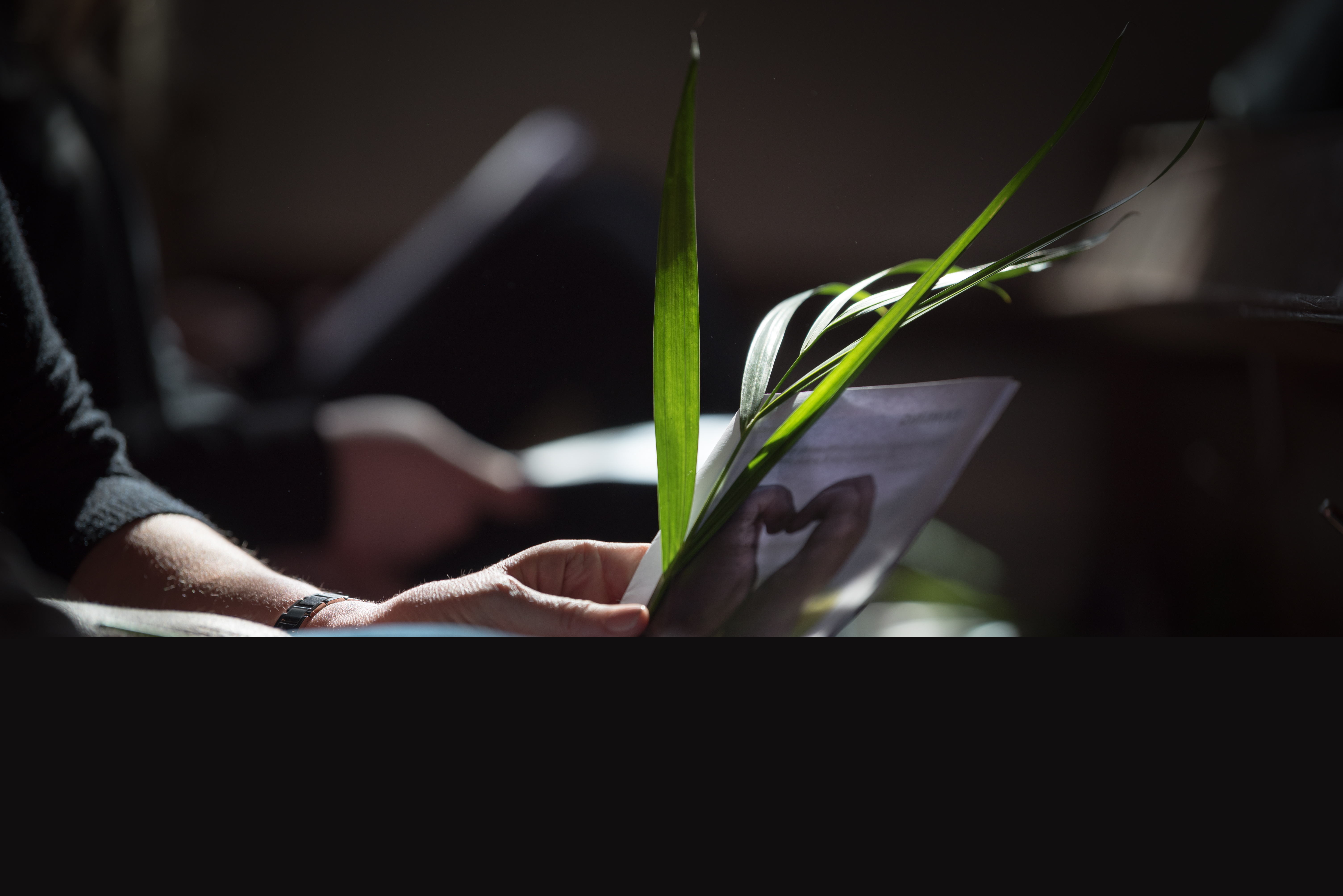 En person sitter med ett palmblad och ett häfte i händerna.