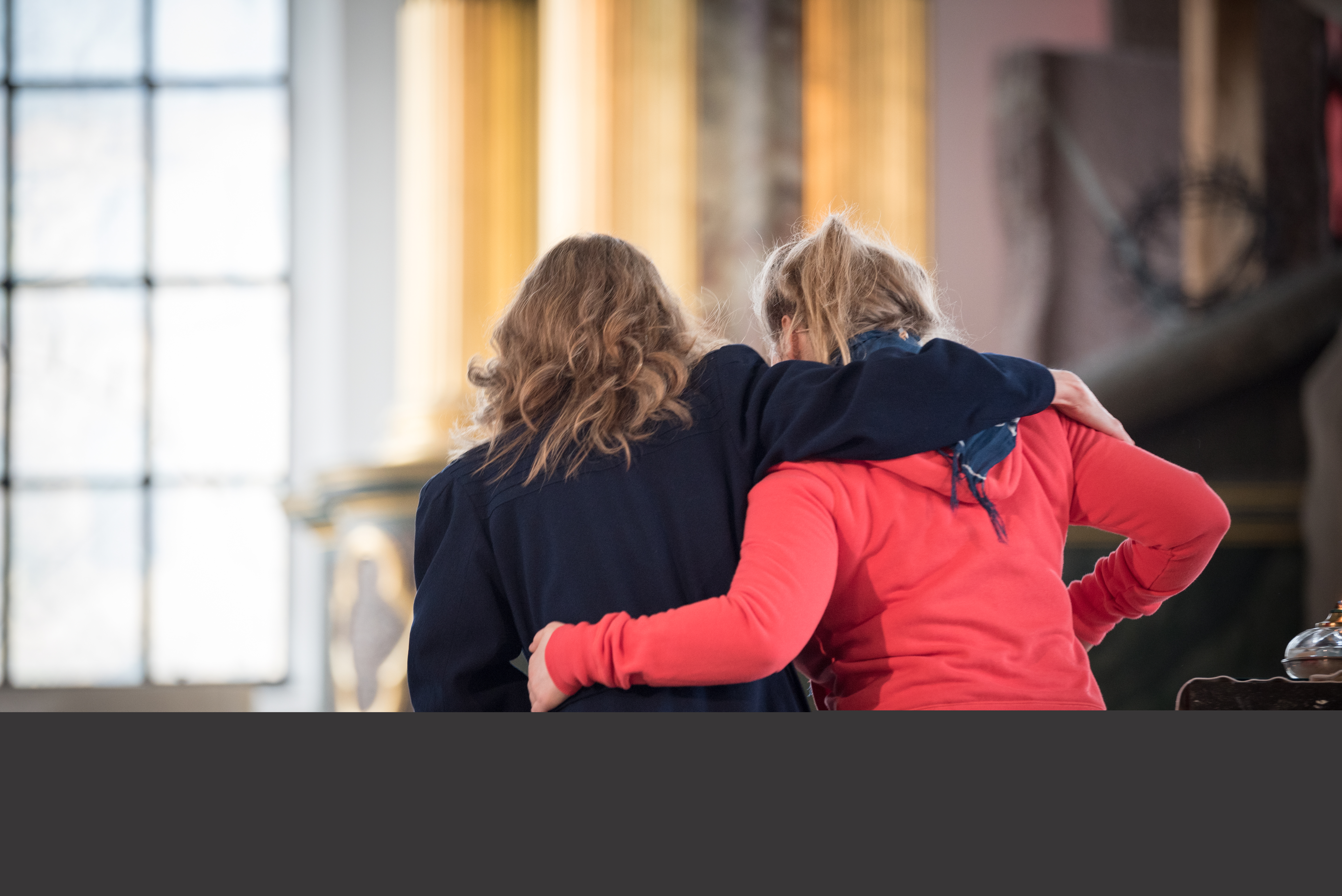 Två kvinnor med armarna om varandra hjälps åt att sätta sig tillrätta i kyrkbänken.