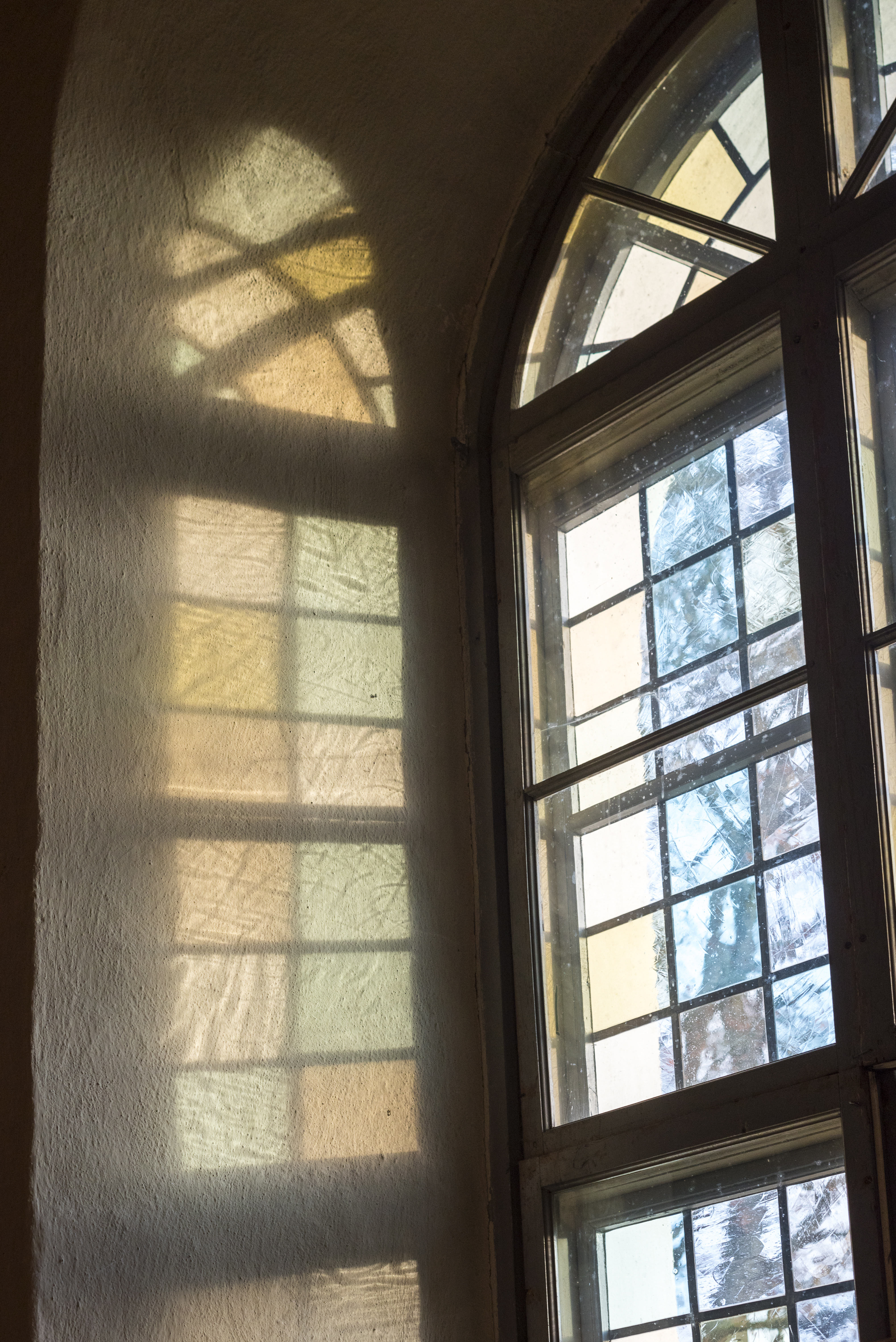 Solen reflekteras på en vit vägg genom ett färgat kyrkfönster.