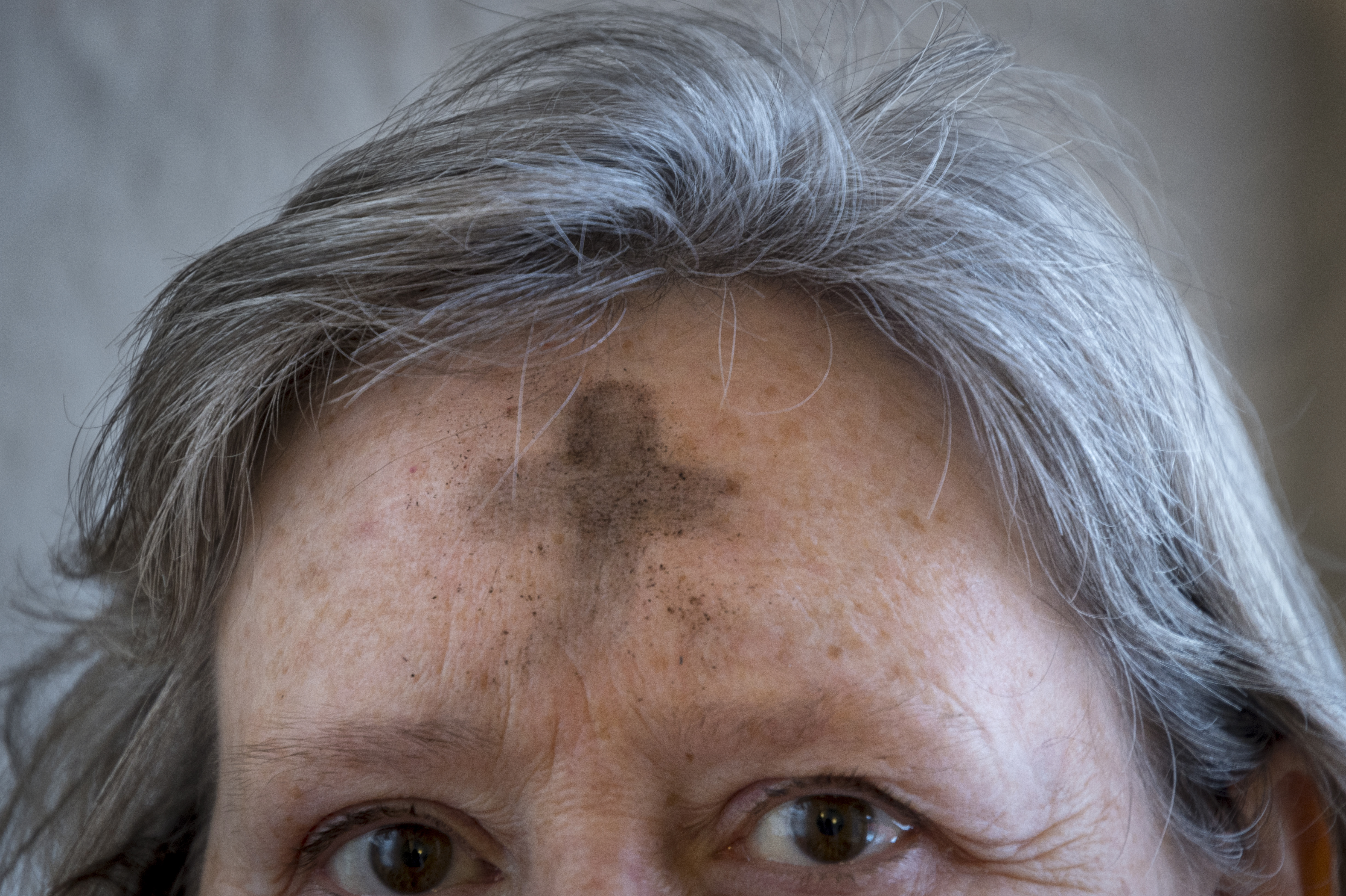 Närbild på en gråhårig kvinna med ett askkors i pannan.