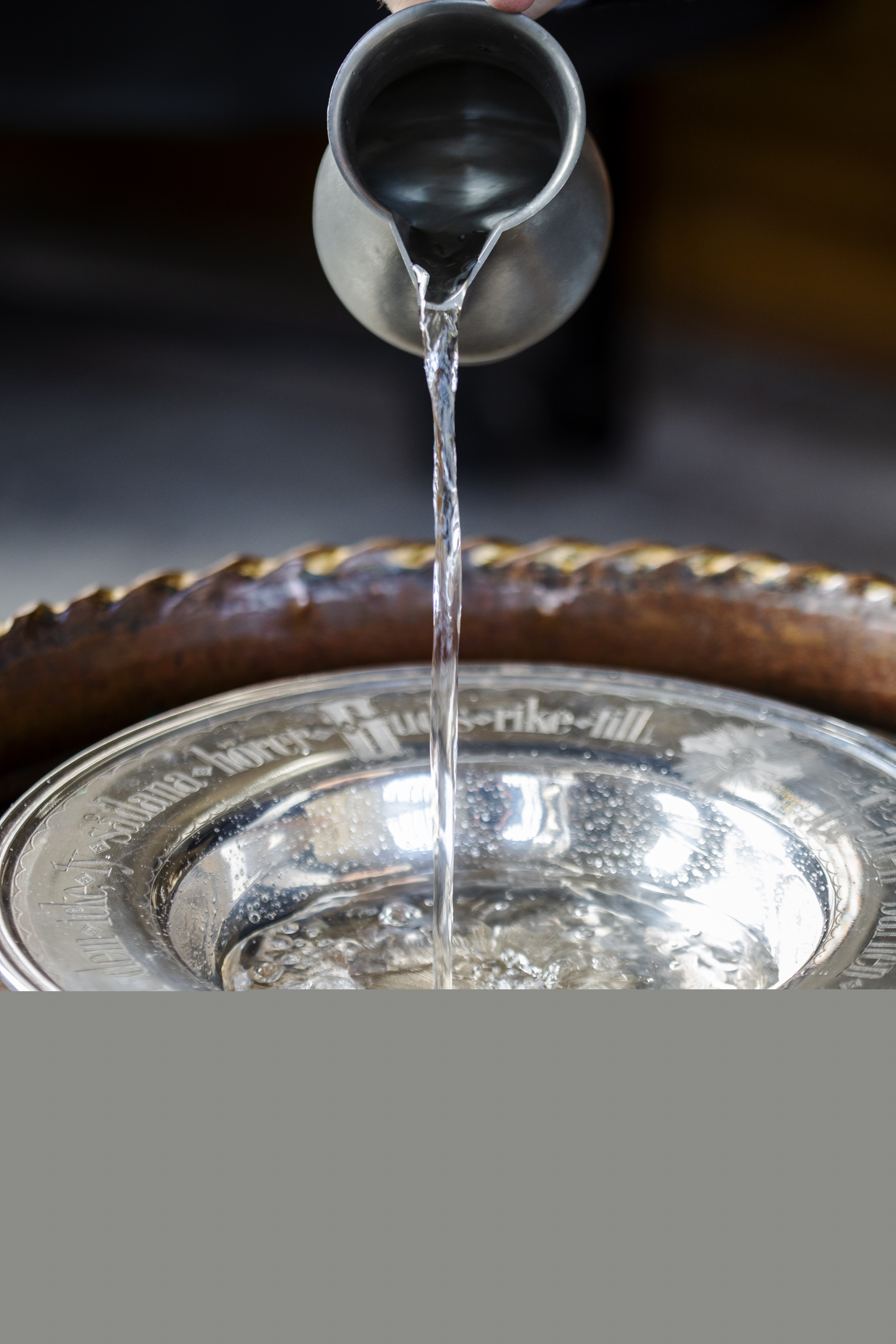 Någon häller vatten i dopfunten från en kanna.