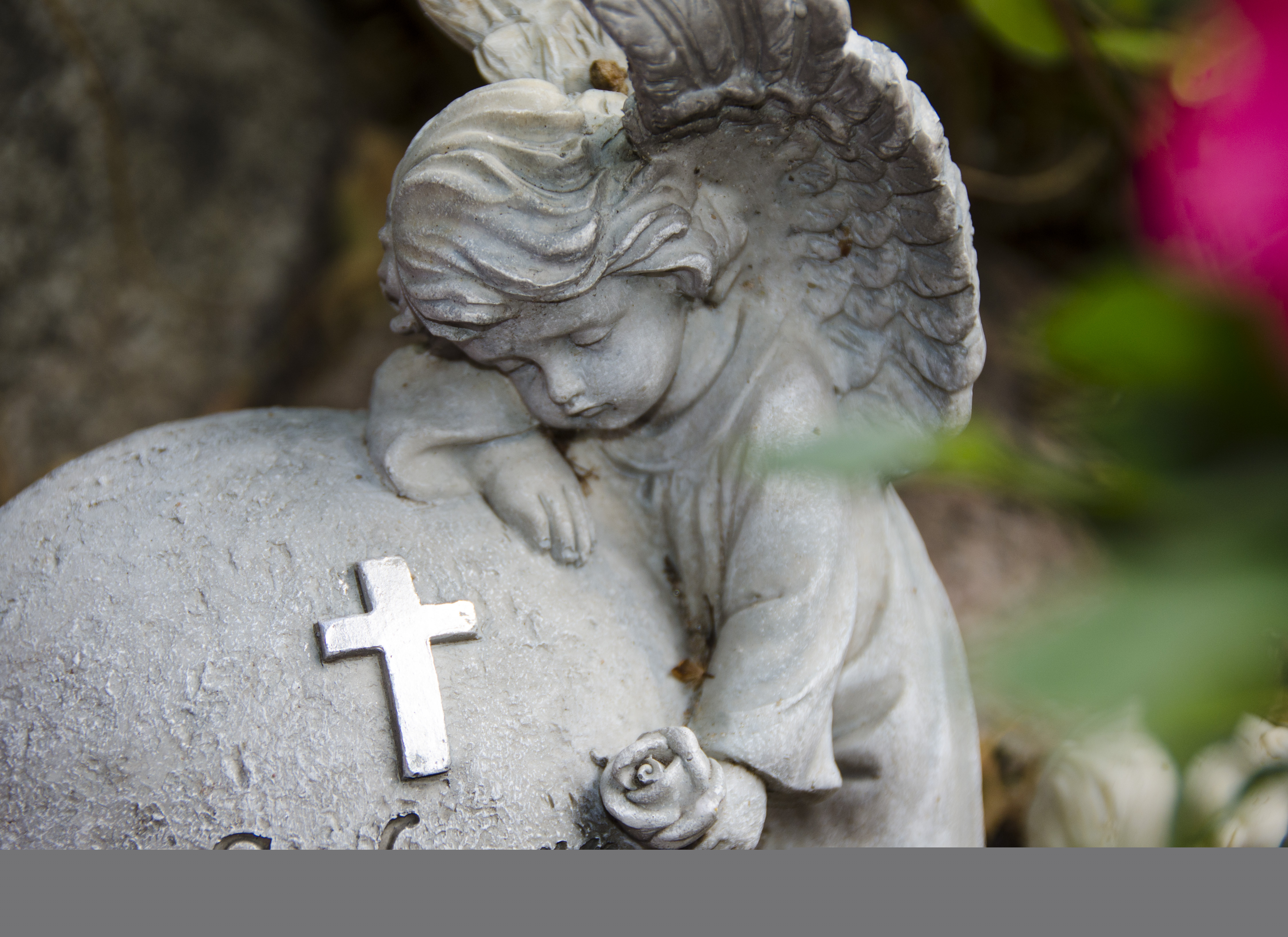 Närbild på en gravdekoration: en ängel kramar om en sten.