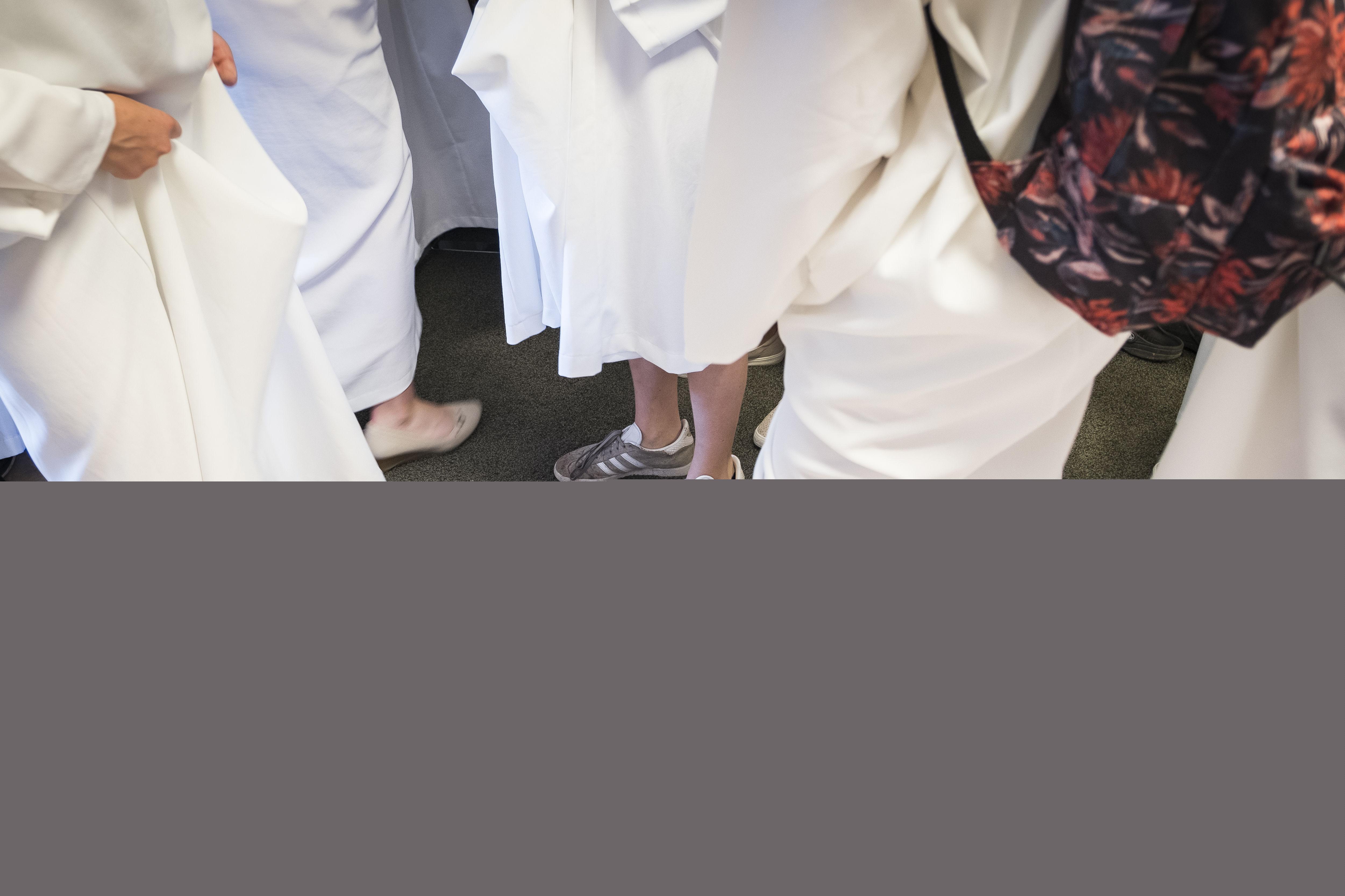 Några konfirmander i vita kåpor jämför sina gympaskor.