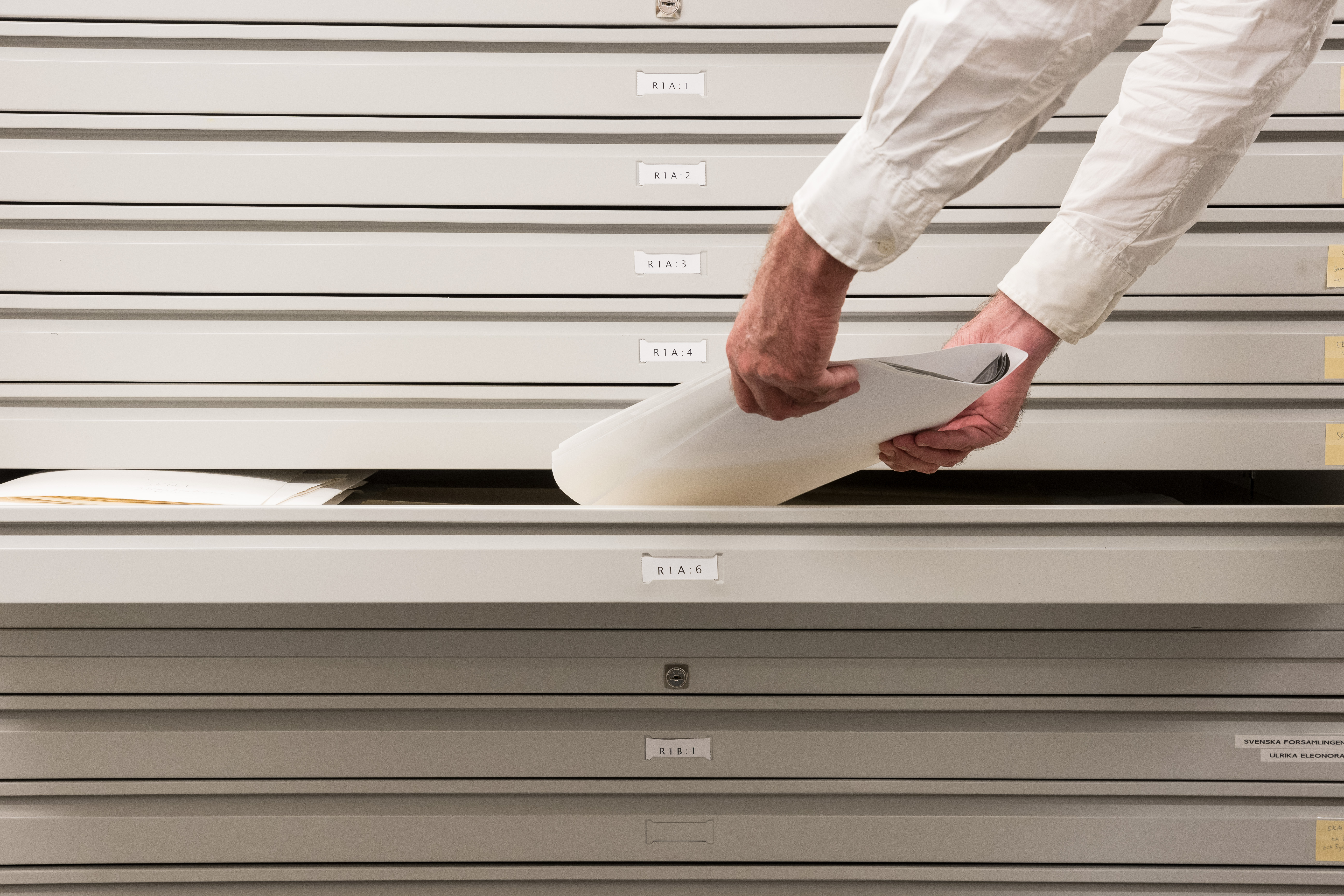 Någon lägger ner papper i en arkivlåda.