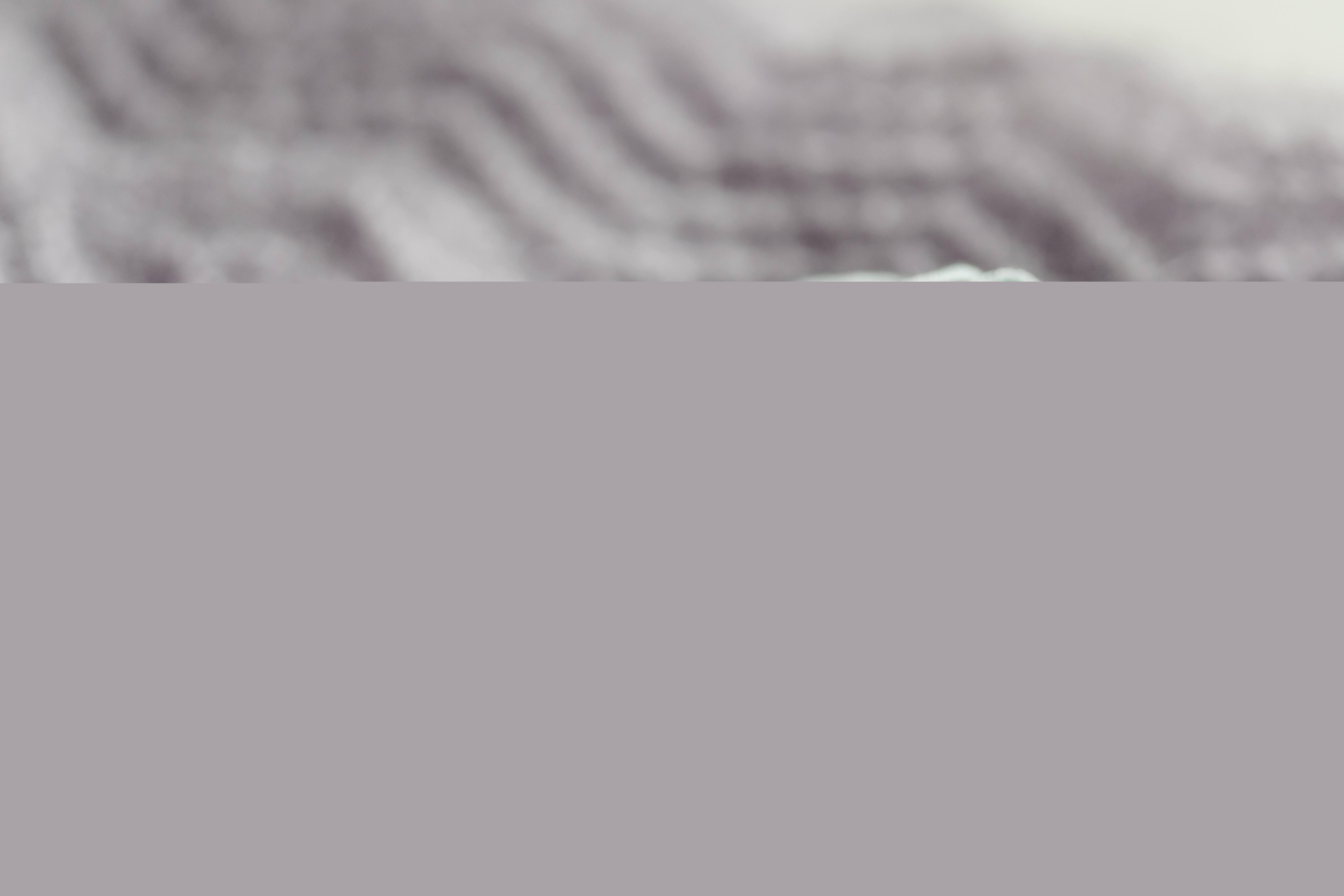 Ett turkost garnnystan och två stickor ligger på en filt.