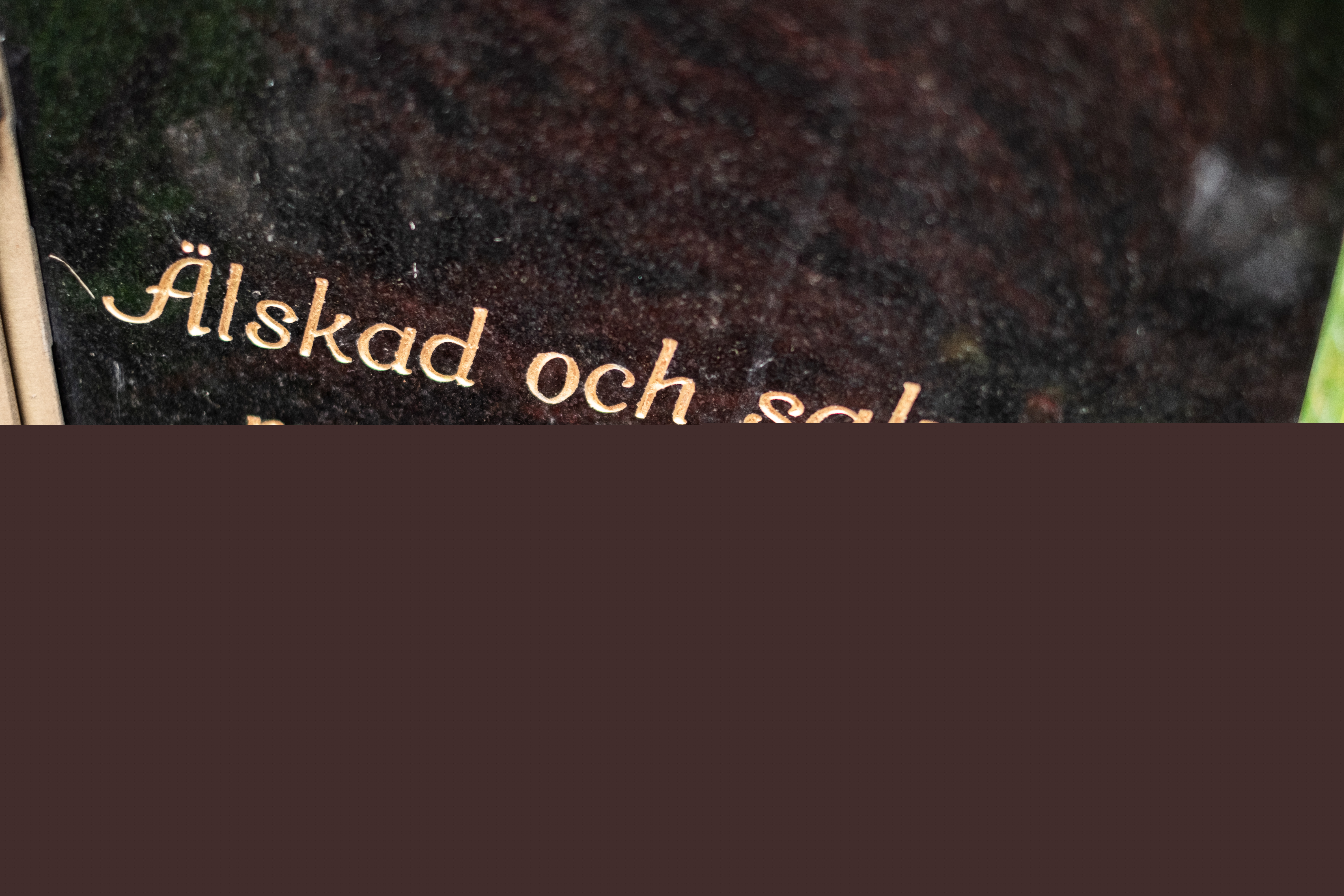 En svart gravsten med guldfärgad text: Älskad och saknad men inte glömd.