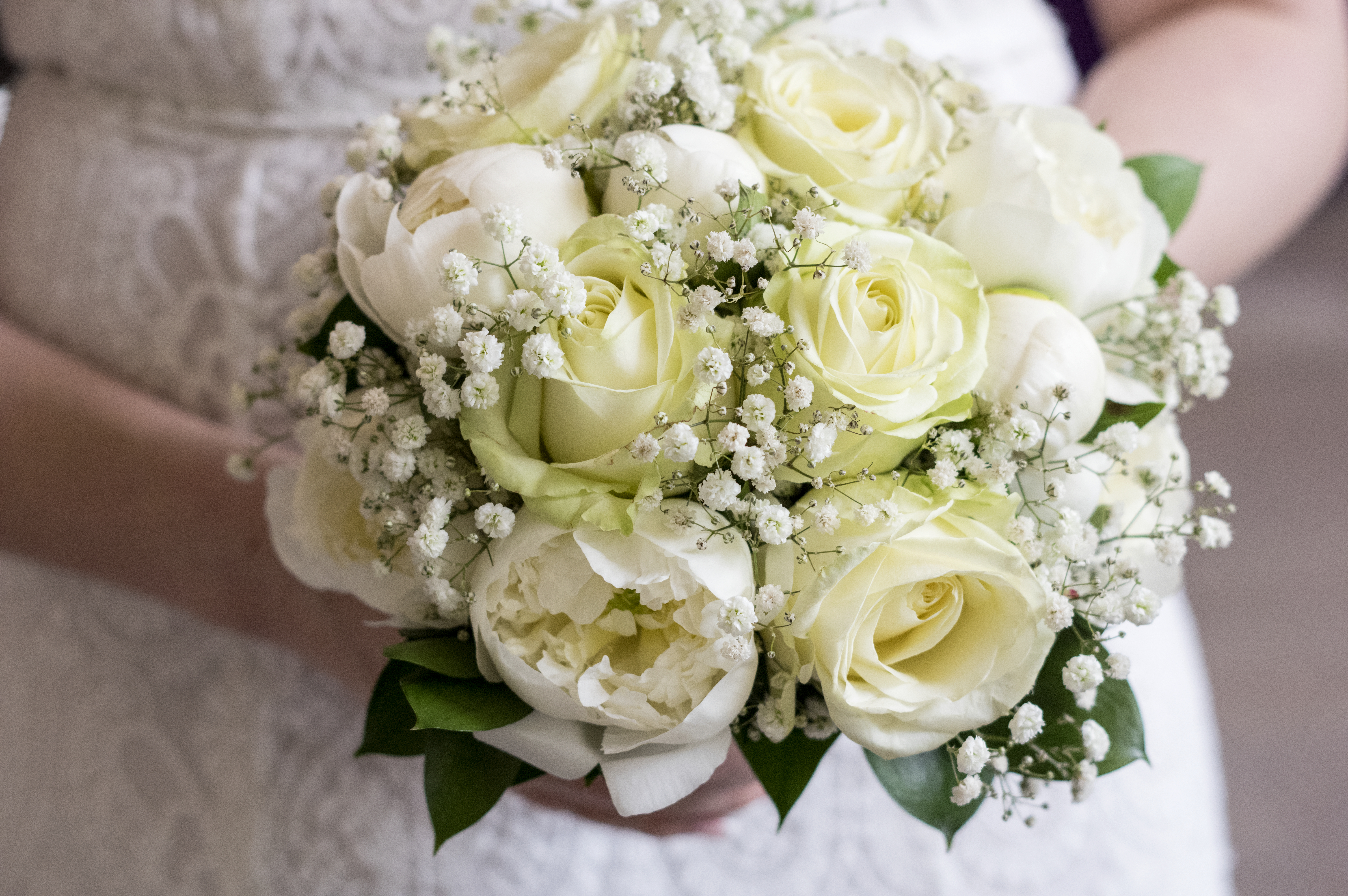 Någon i vit klänning håller en bukett vita rosor.