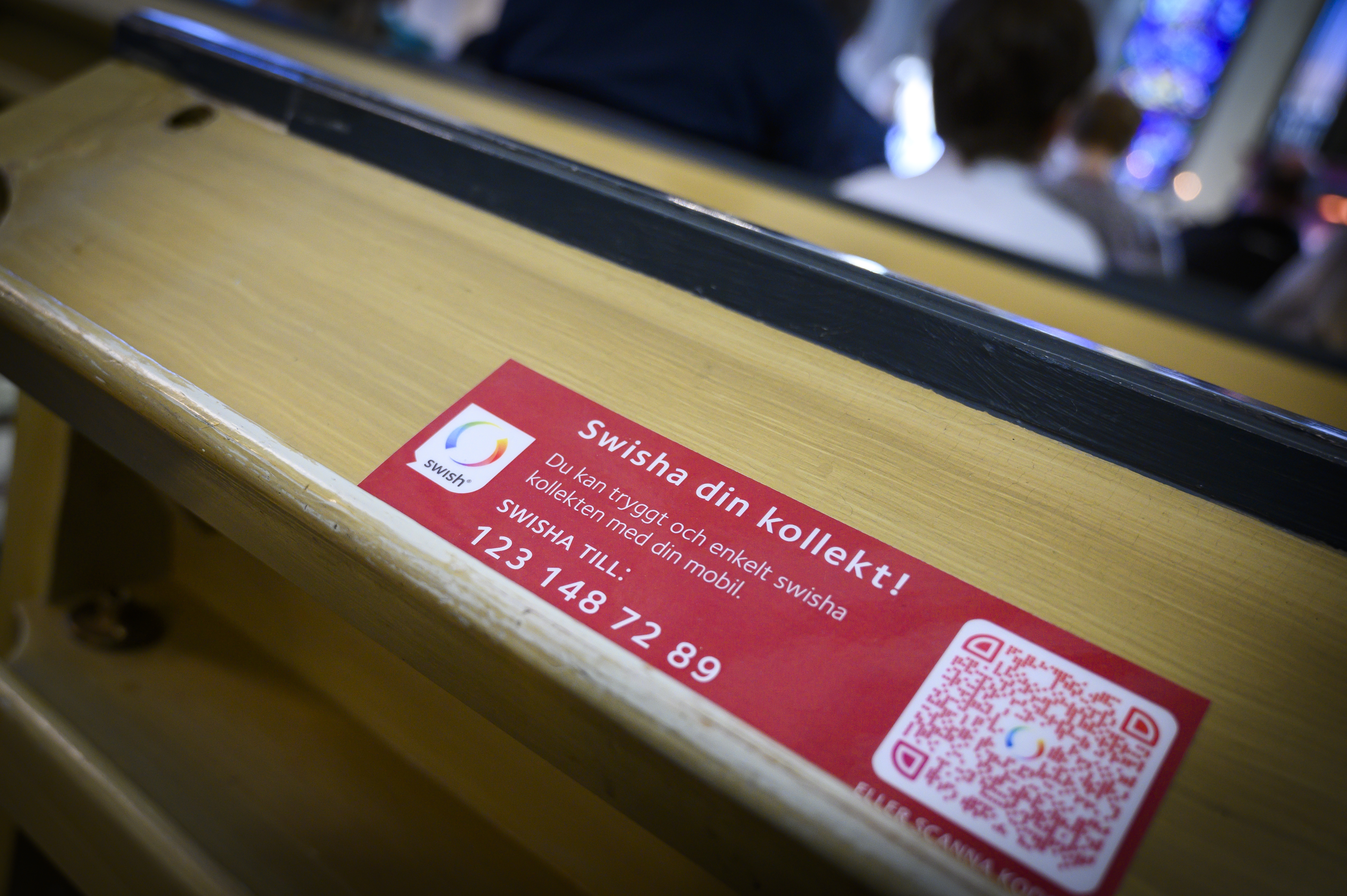 En lapp med texten Swisha din kollekt ligger i en kyrkbänk.