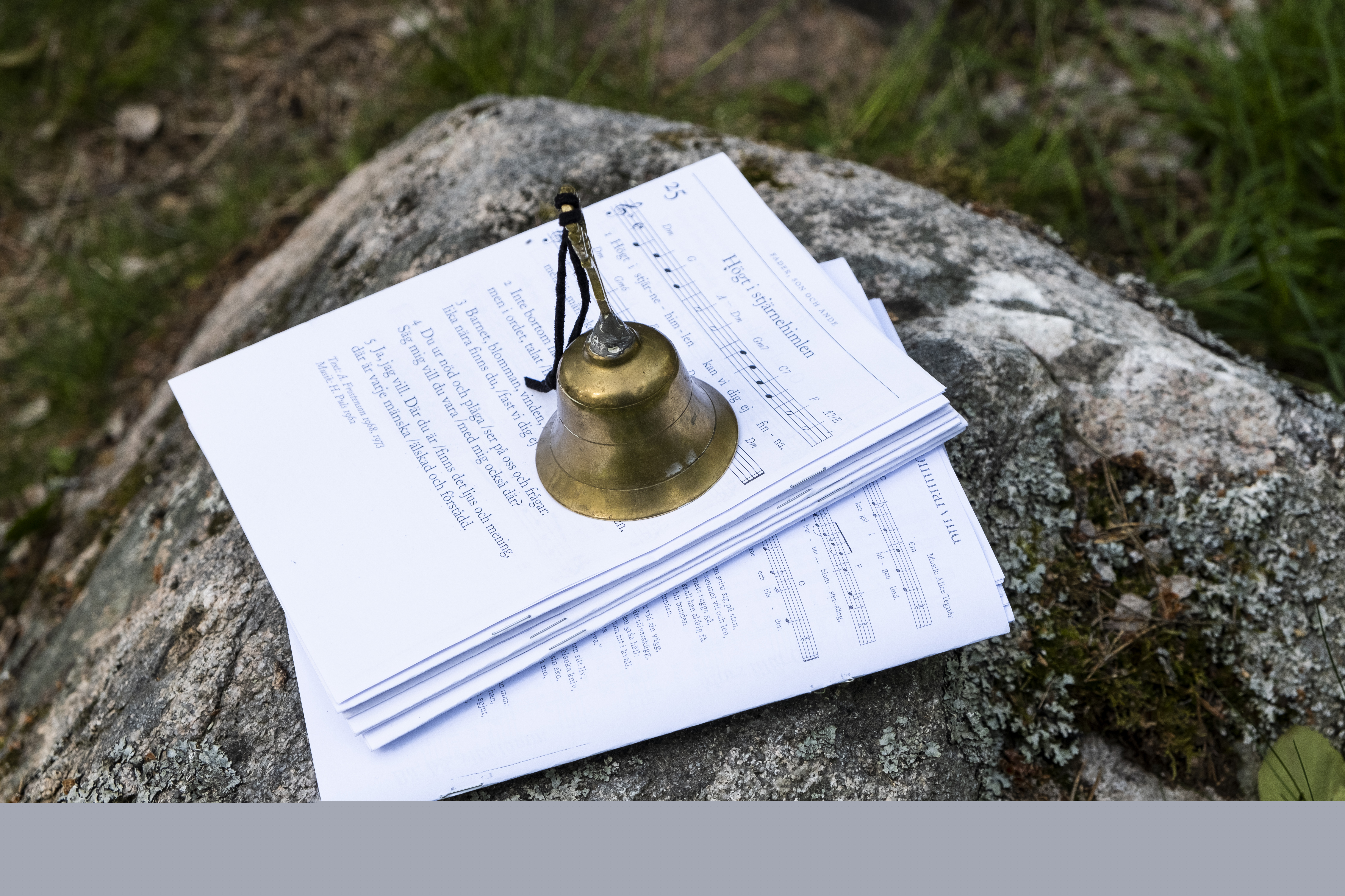 På en sten ligger notpapper. En ringklocka står ovanpå så de inte blåser iväg.