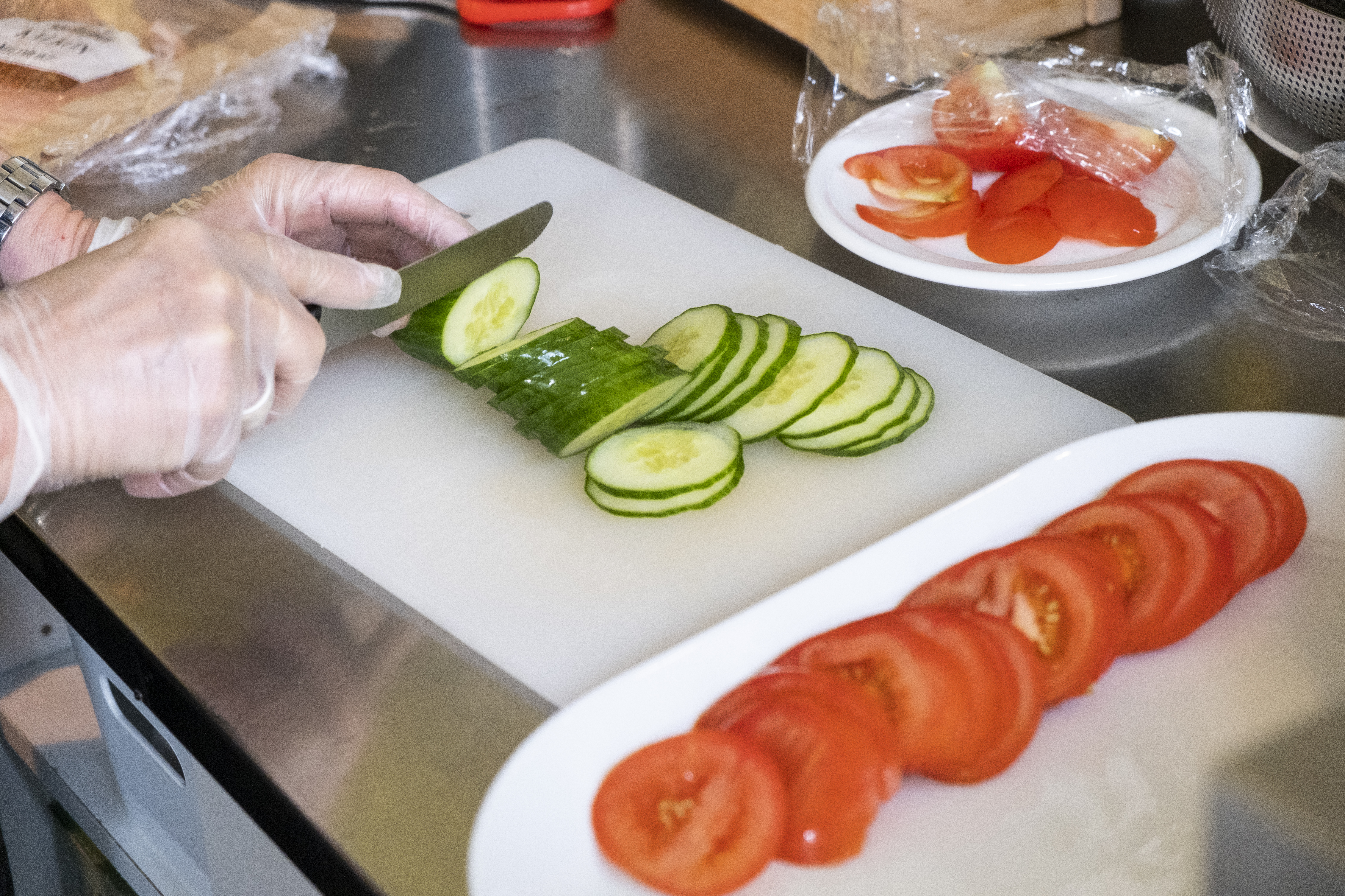 Någon skär upp gurka och tomat och lägger upp på fat.
