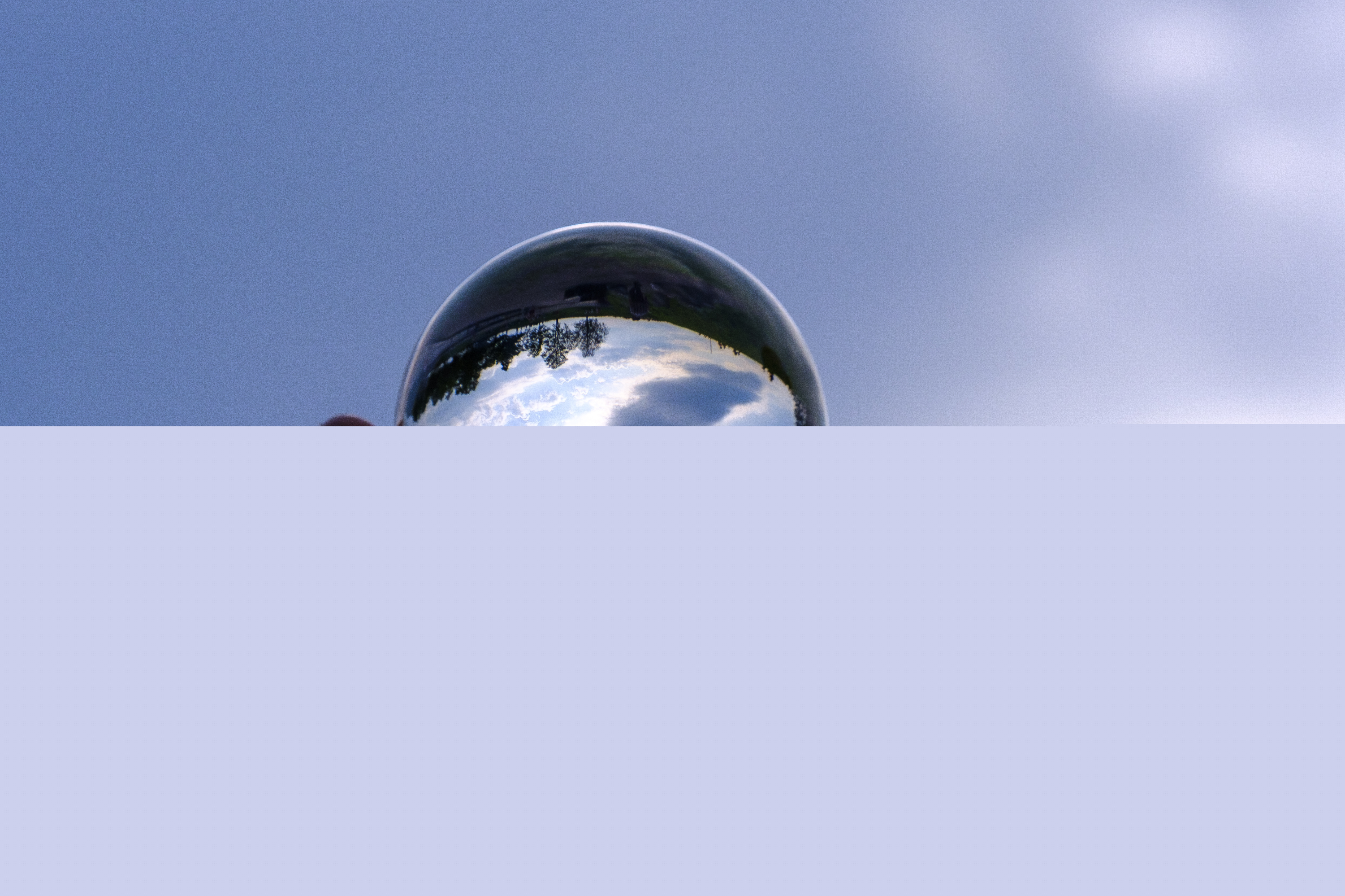 En kupad hand håller ett glasklot. Blå himmel i bakgrunden.