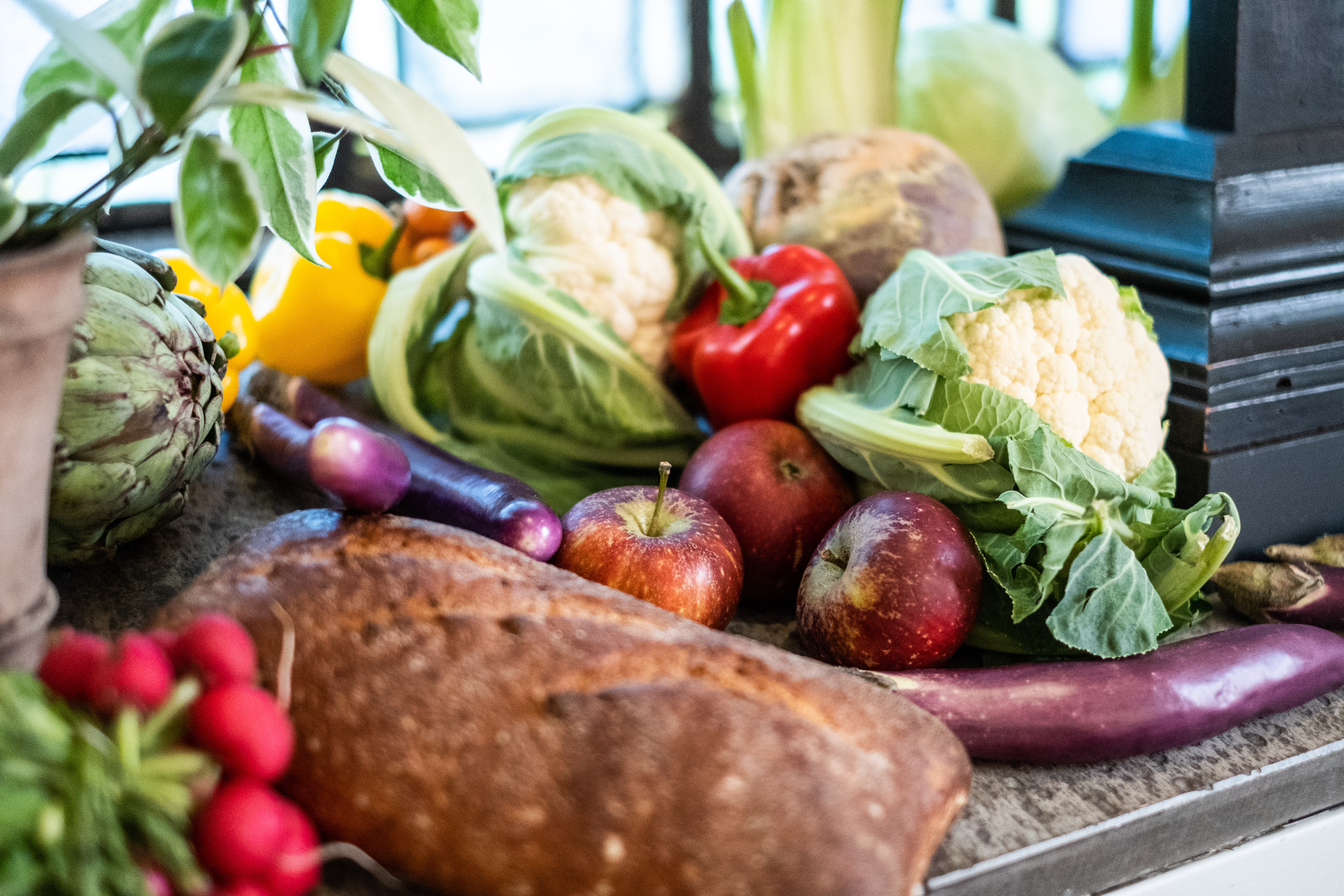 En hög med grönsaker, frukter och bröd ligger i ett fönster.