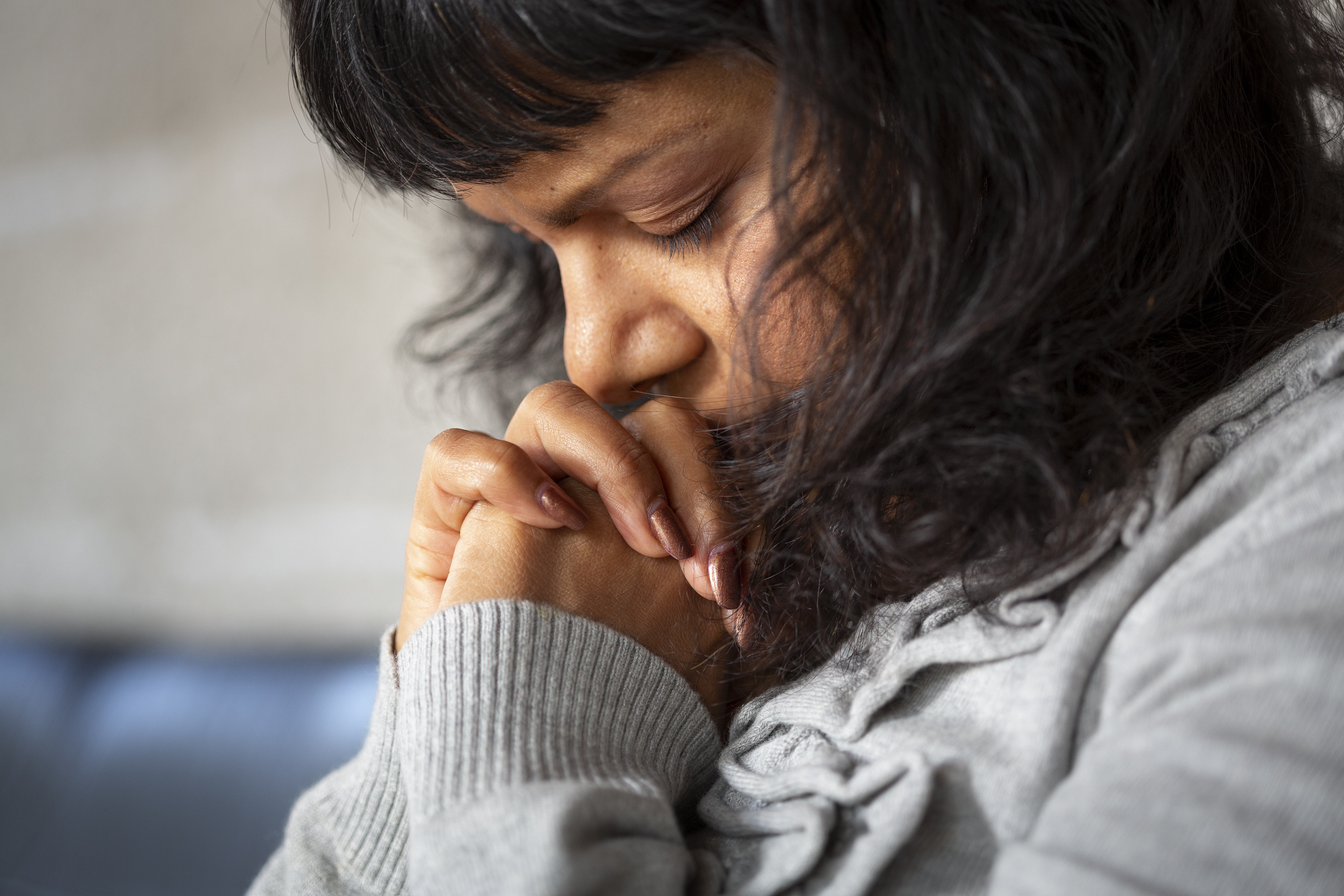 En kvinna som blundar har fört sina knäppta händer till sitt ansikte.