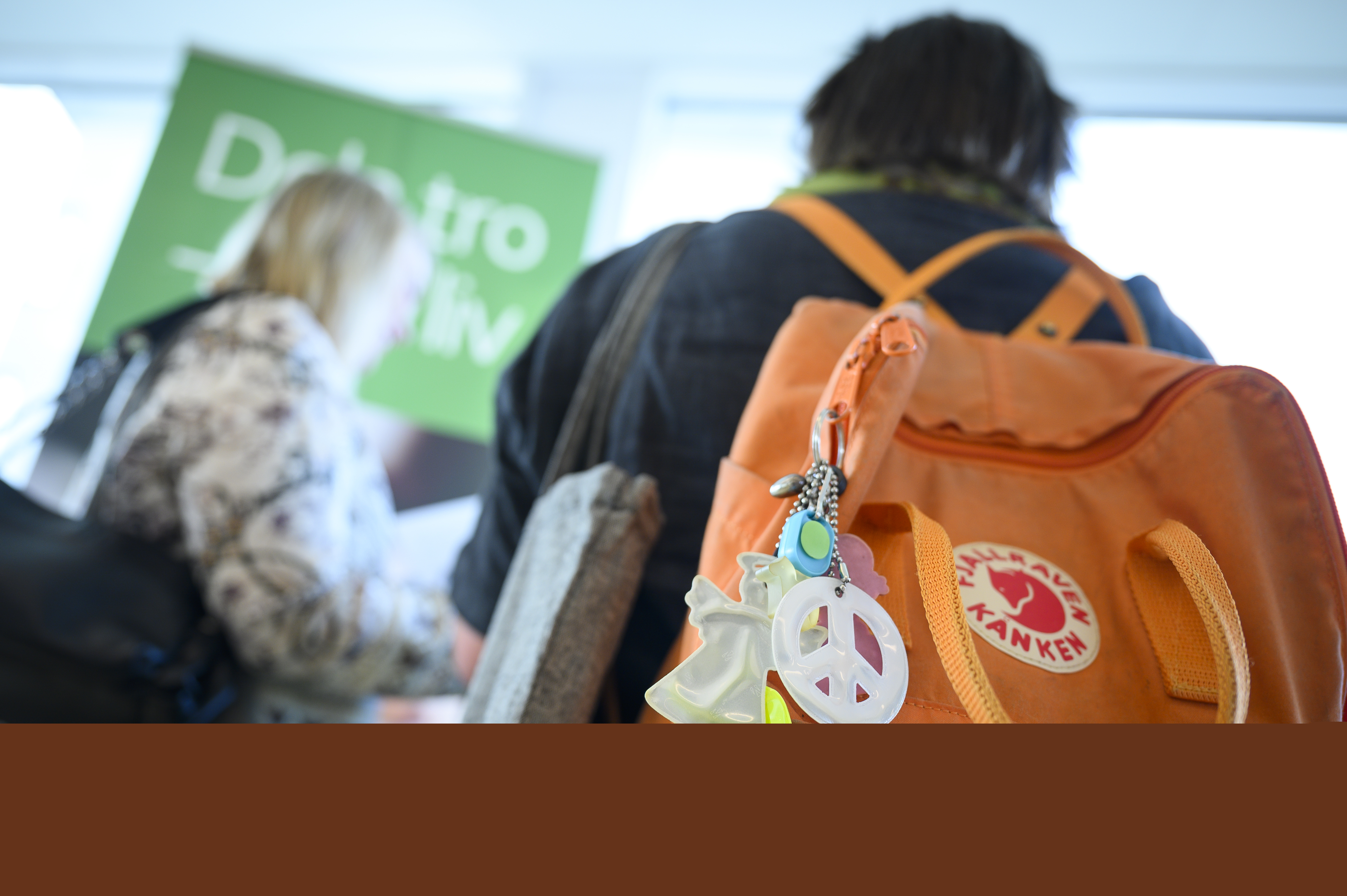 Två personer på konferens eller mässa. Personen närmast kameran har en ryggsäck med olika reflexer hängande.